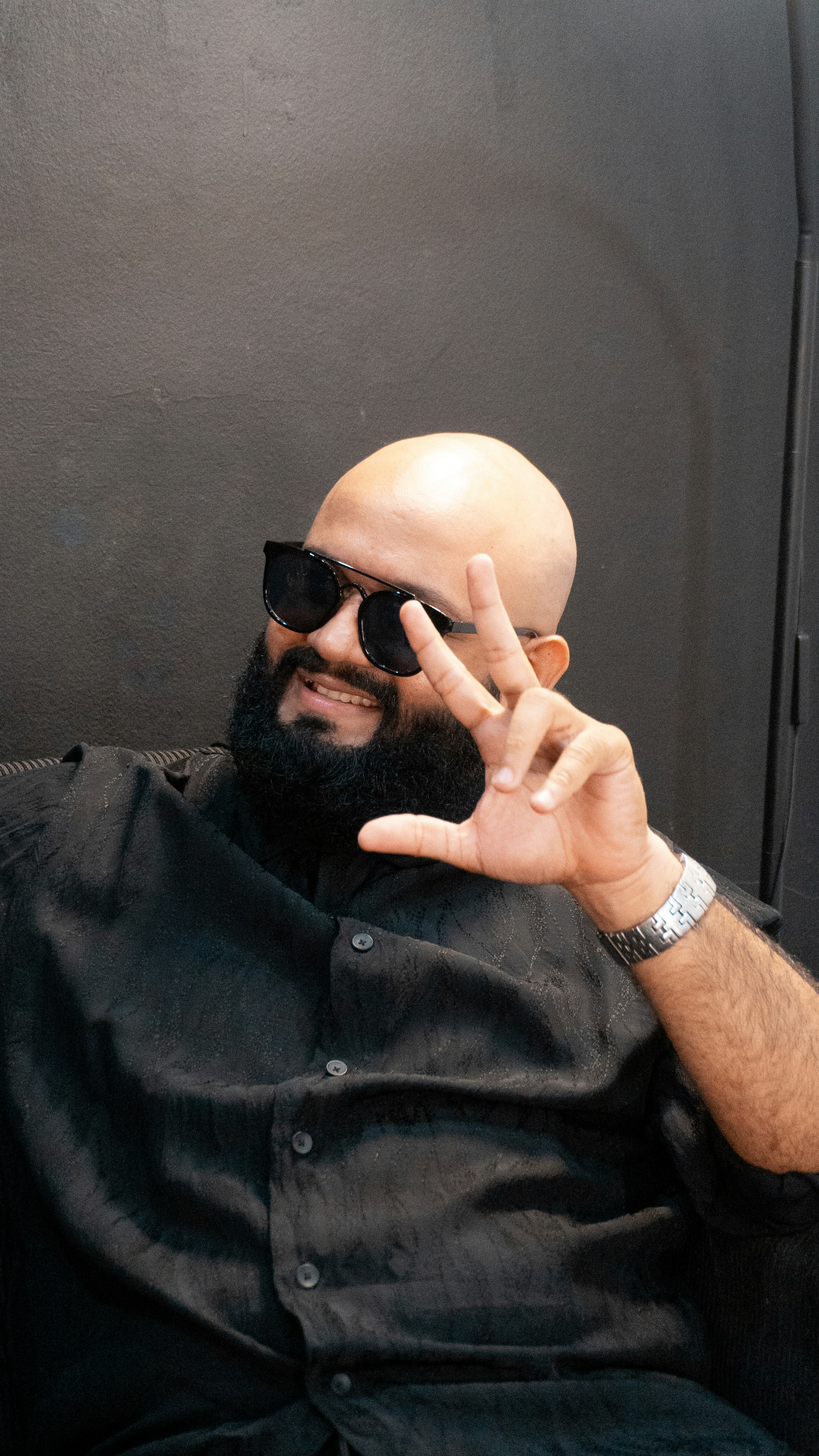 Bald man with beard wearing sunglasses and black shirt.