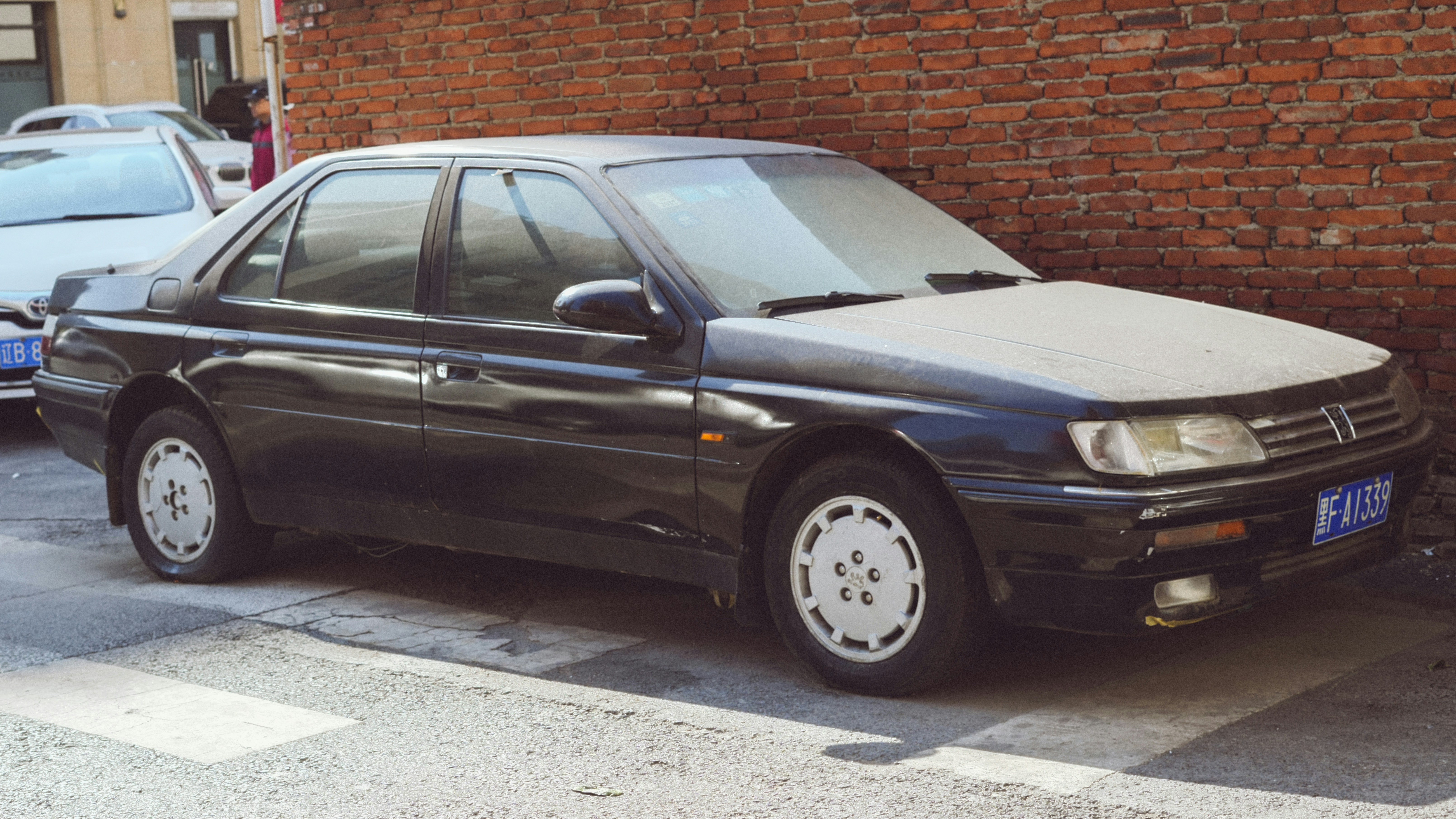 A dark sedan parked against a brick wall.
