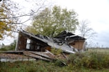 A dilapidated wooden house collapsing in a field.