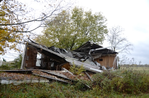 A dilapidated wooden house collapsing in a field.