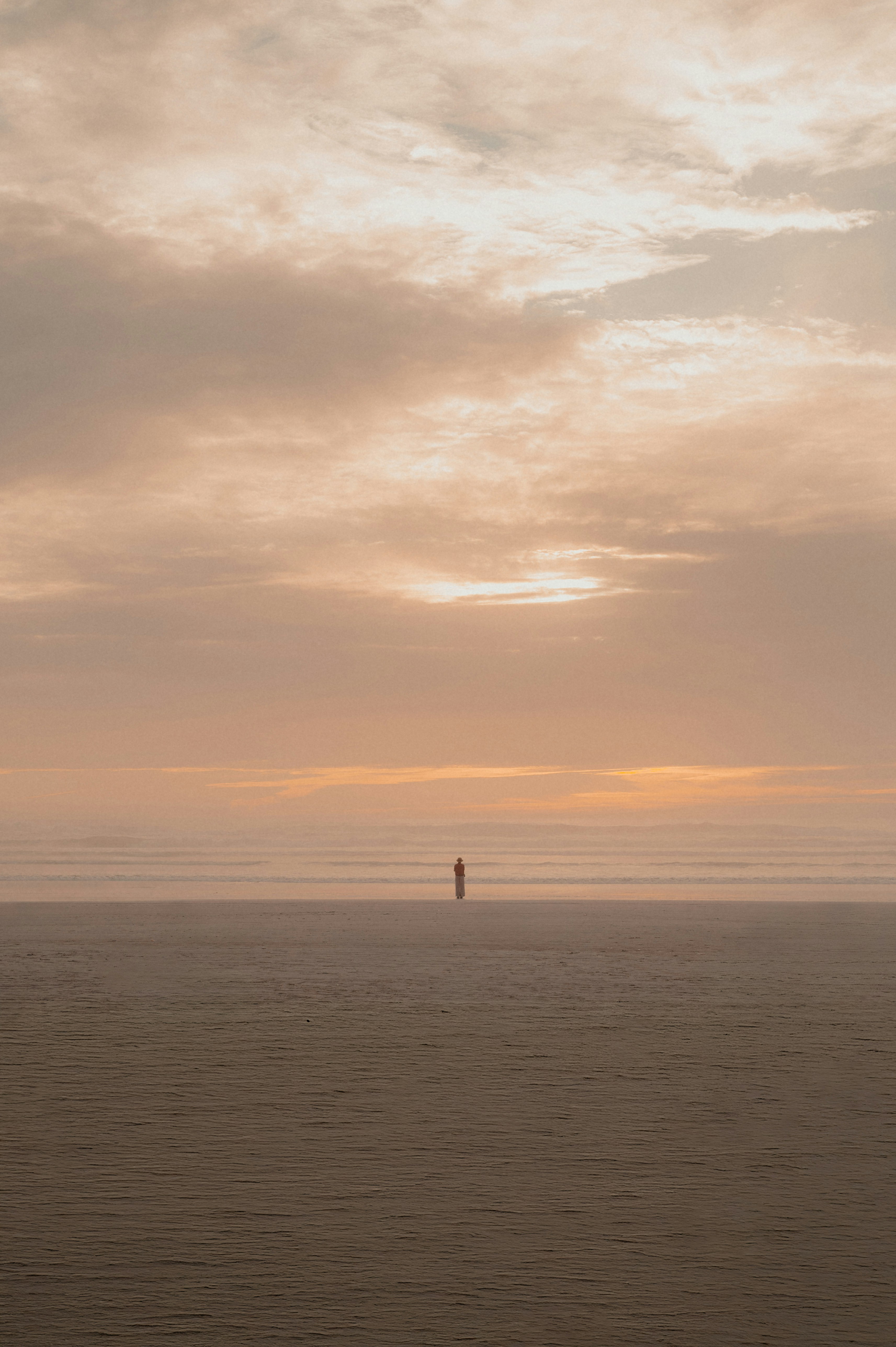 A lone figure stands on a vast beach at sunset.