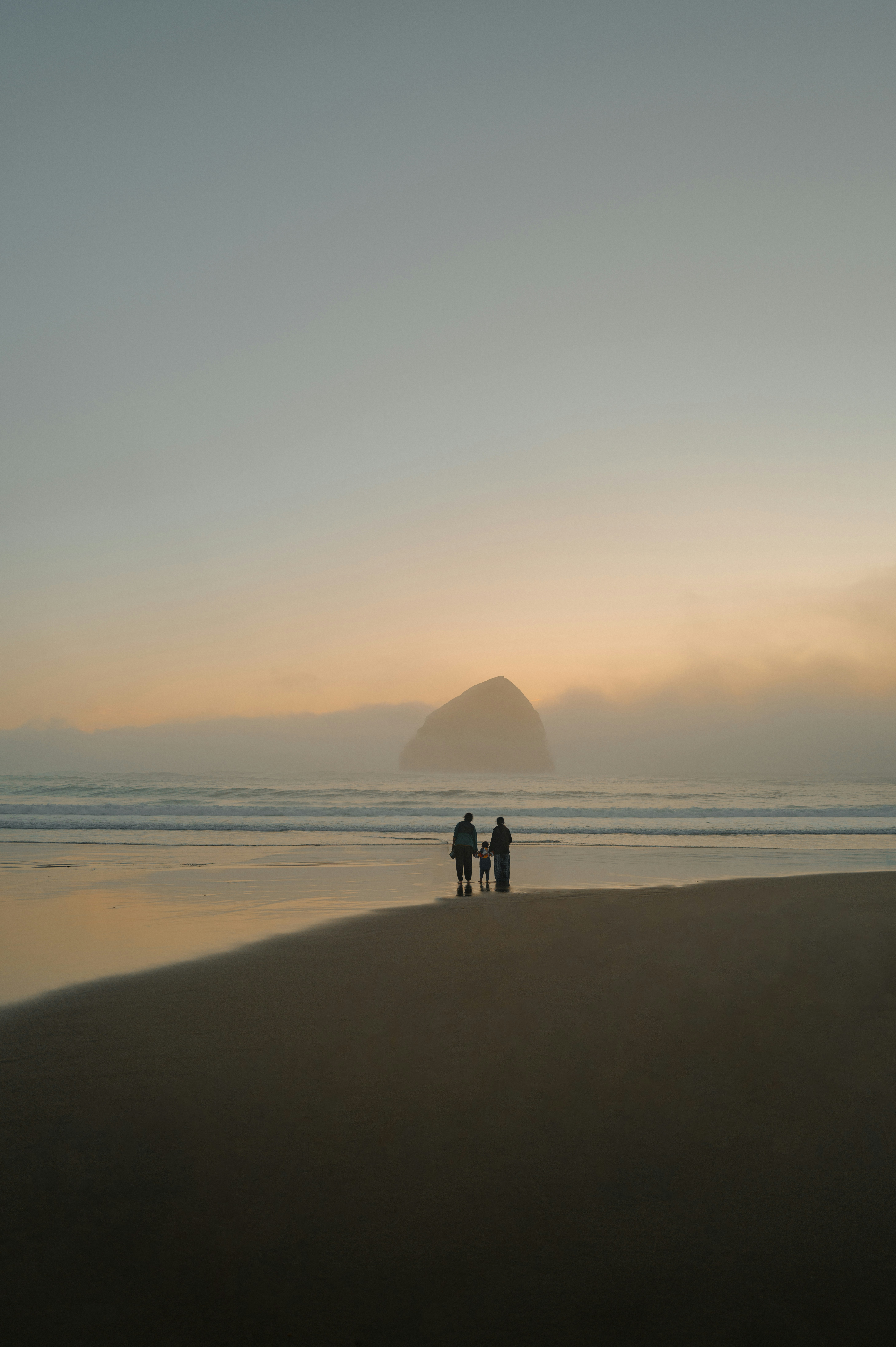 Two figures stand on a misty beach at sunset.