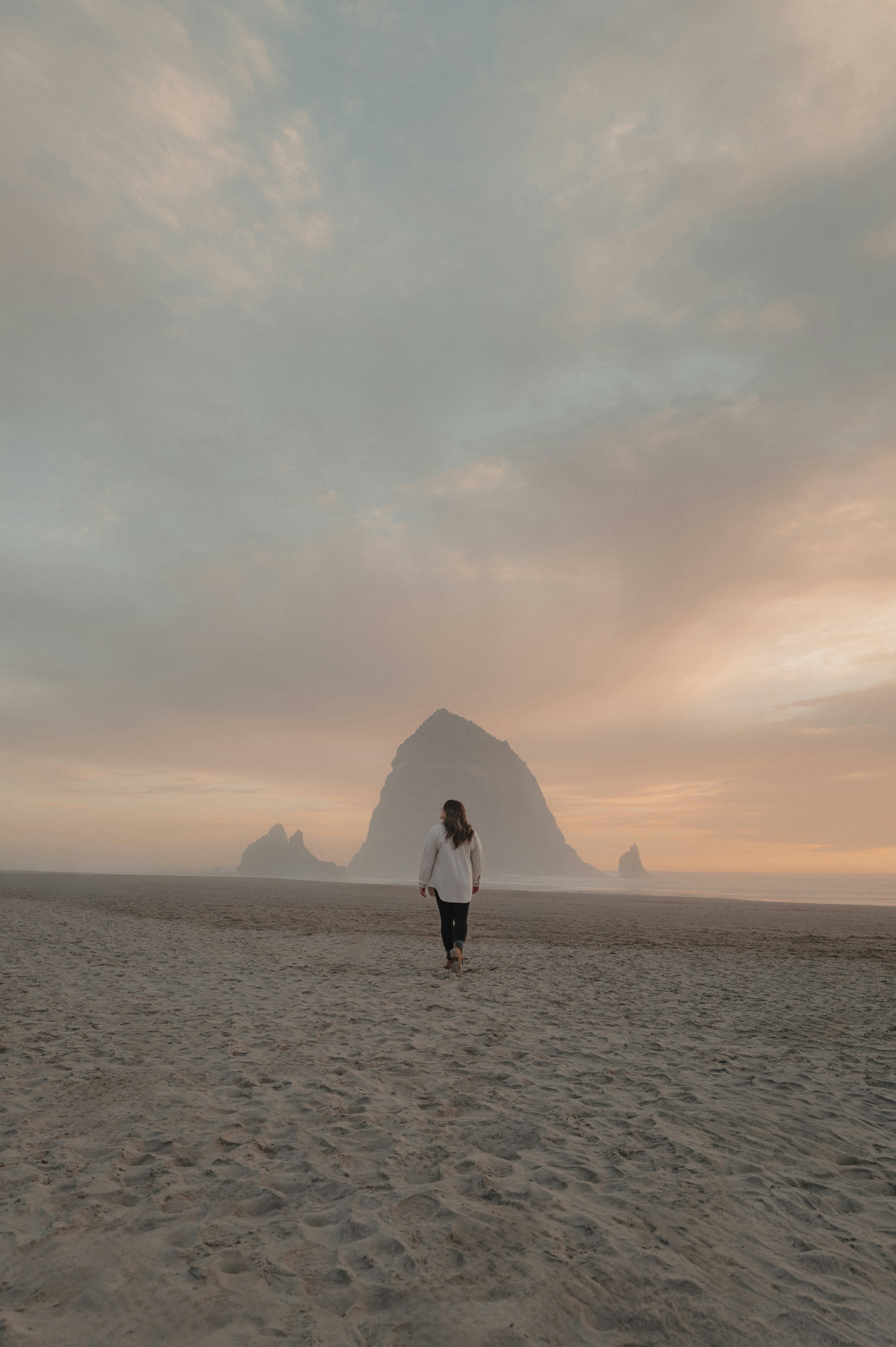 Donna che cammina sulla spiaggia verso una grande formazione rocciosa.