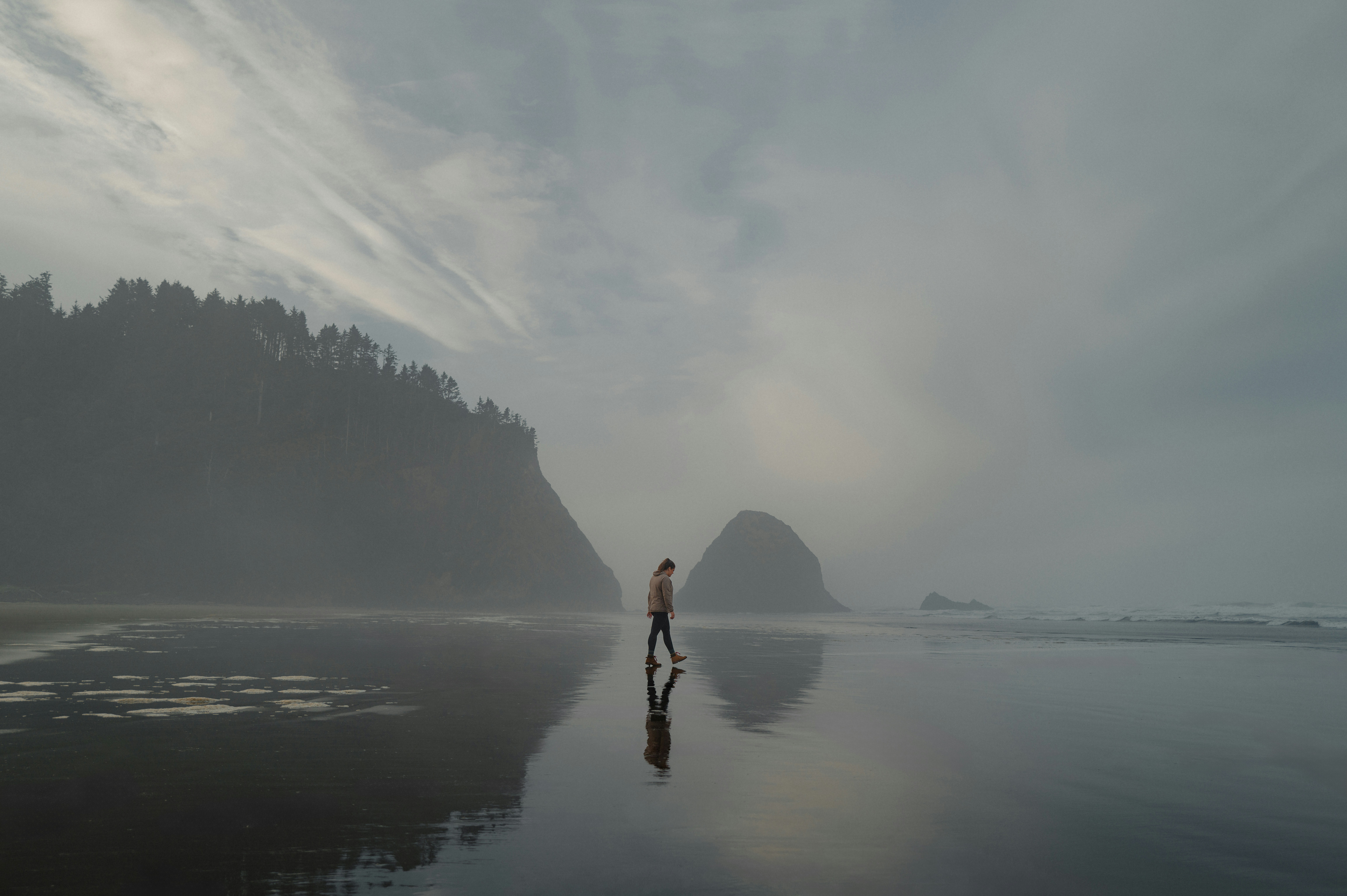 Persona che cammina su una spiaggia nebbiosa con riflessi.