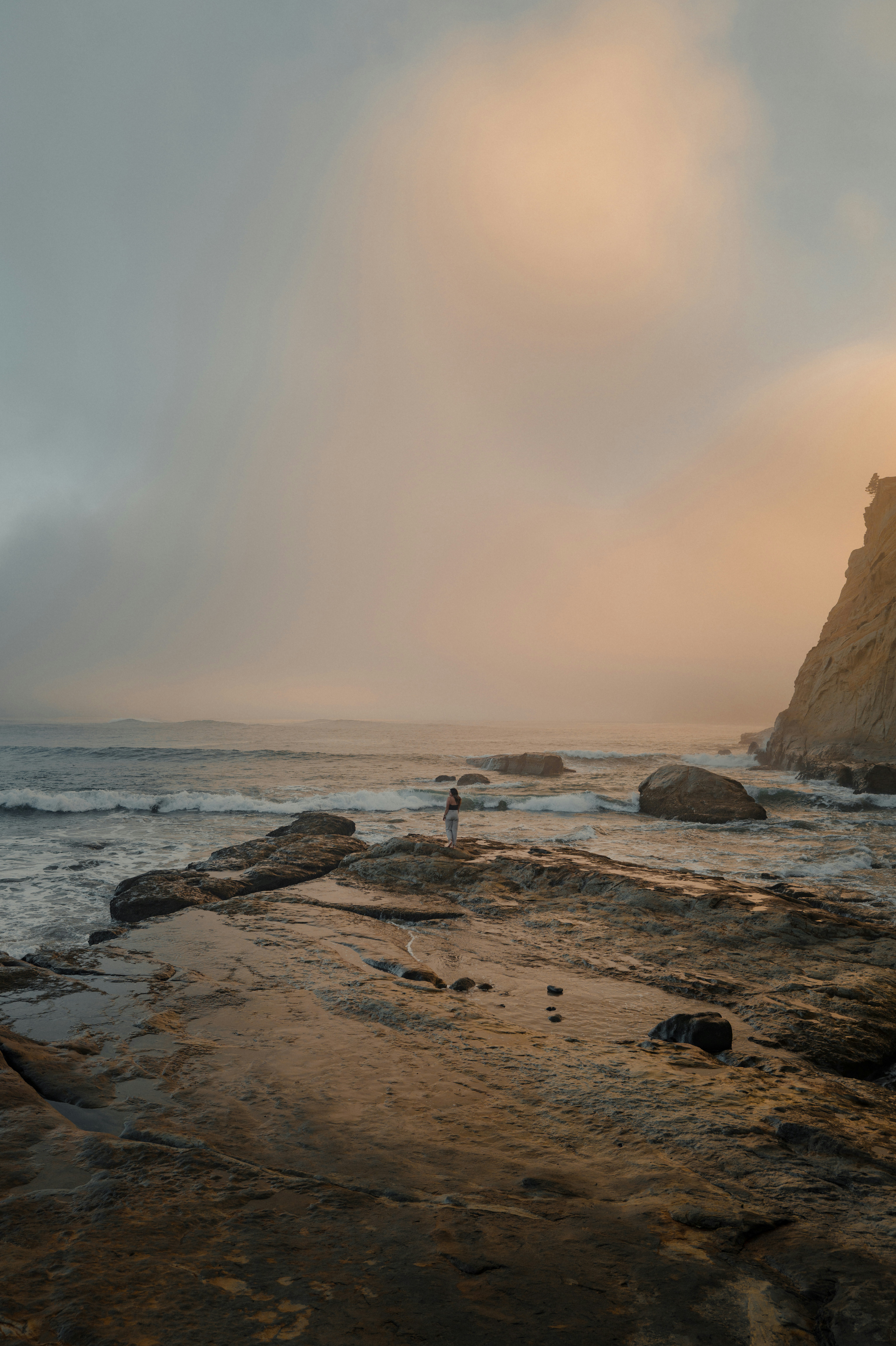 Una persona si trova su una costa rocciosa con le onde dell'oceano.
