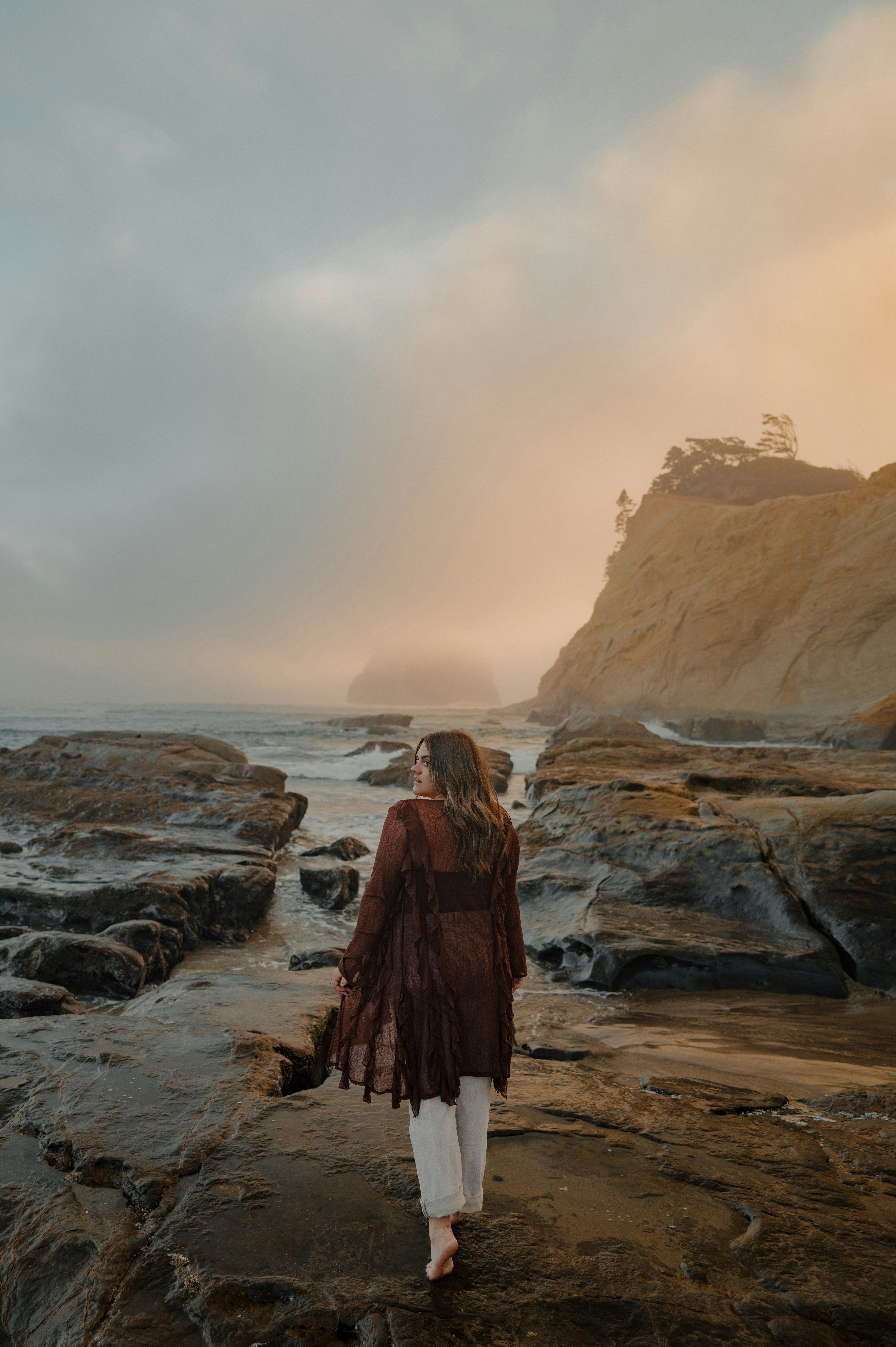 Donna che cammina sulla costa rocciosa verso l'oceano nebbioso