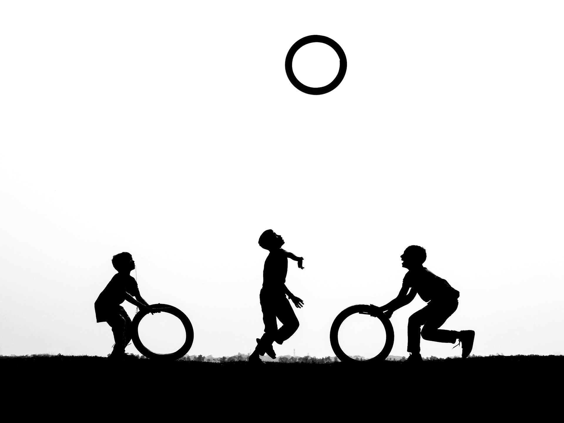 Children playing with hoops against a bright sky