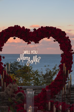 Heart-shaped floral arch with proposal sign at sunset