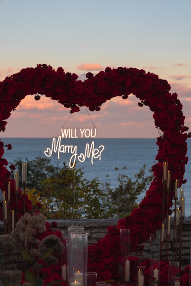 Heart-shaped floral arch with proposal sign at sunset