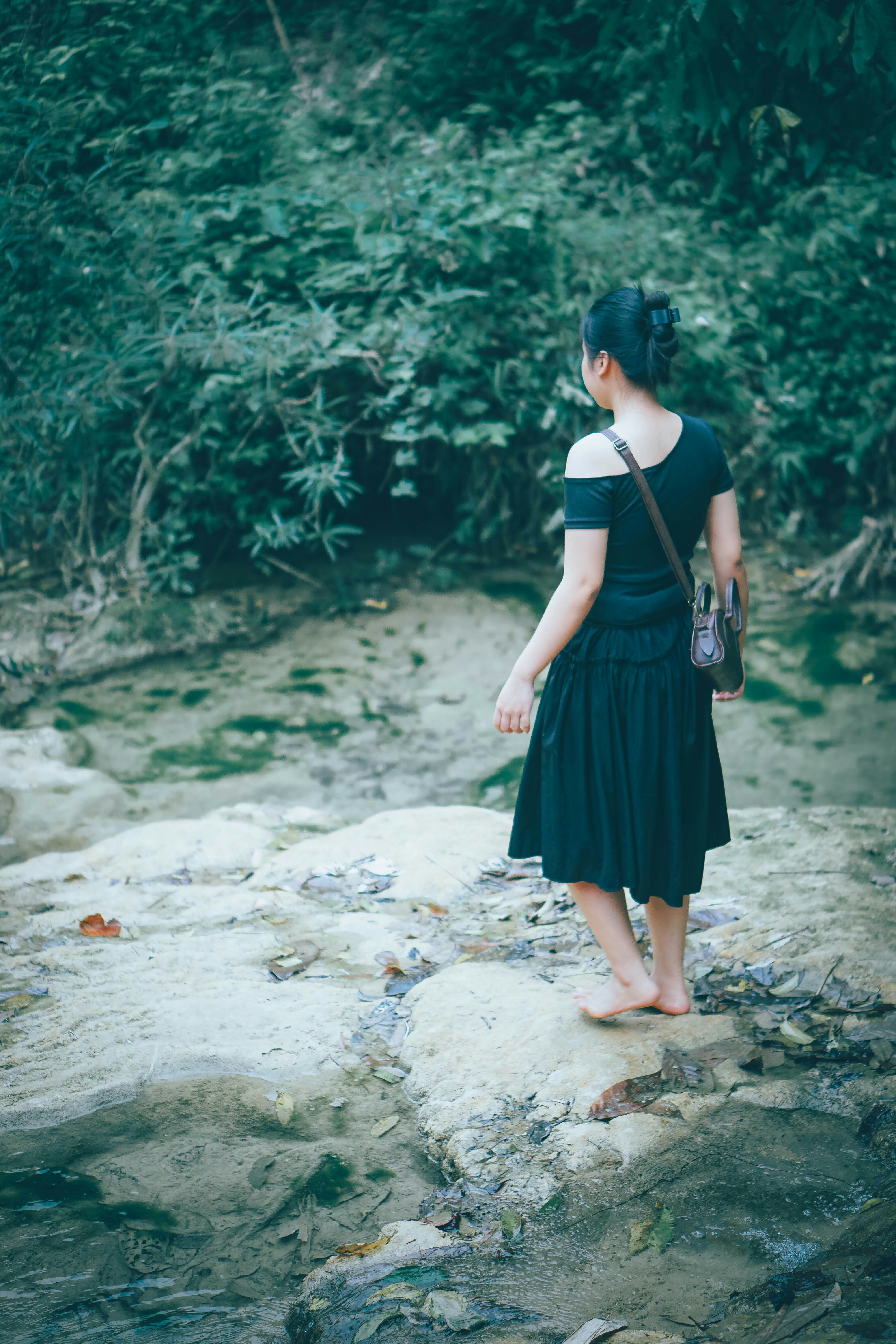 A woman stands by a shallow stream in a forest.