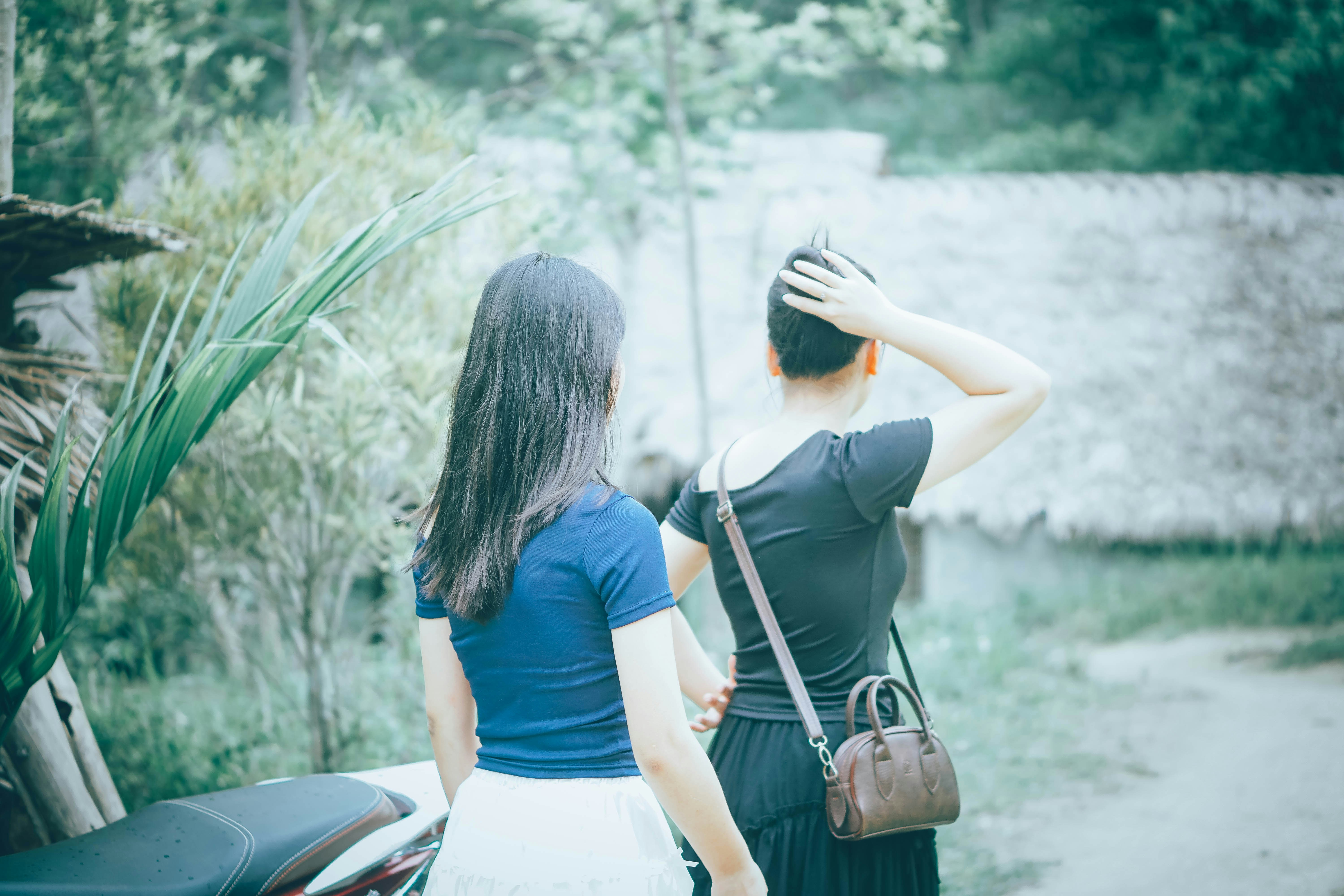 Two women walking outdoors with trees and huts.