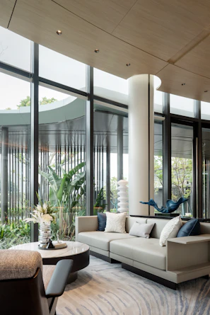 Modern living room with large windows and lush greenery.