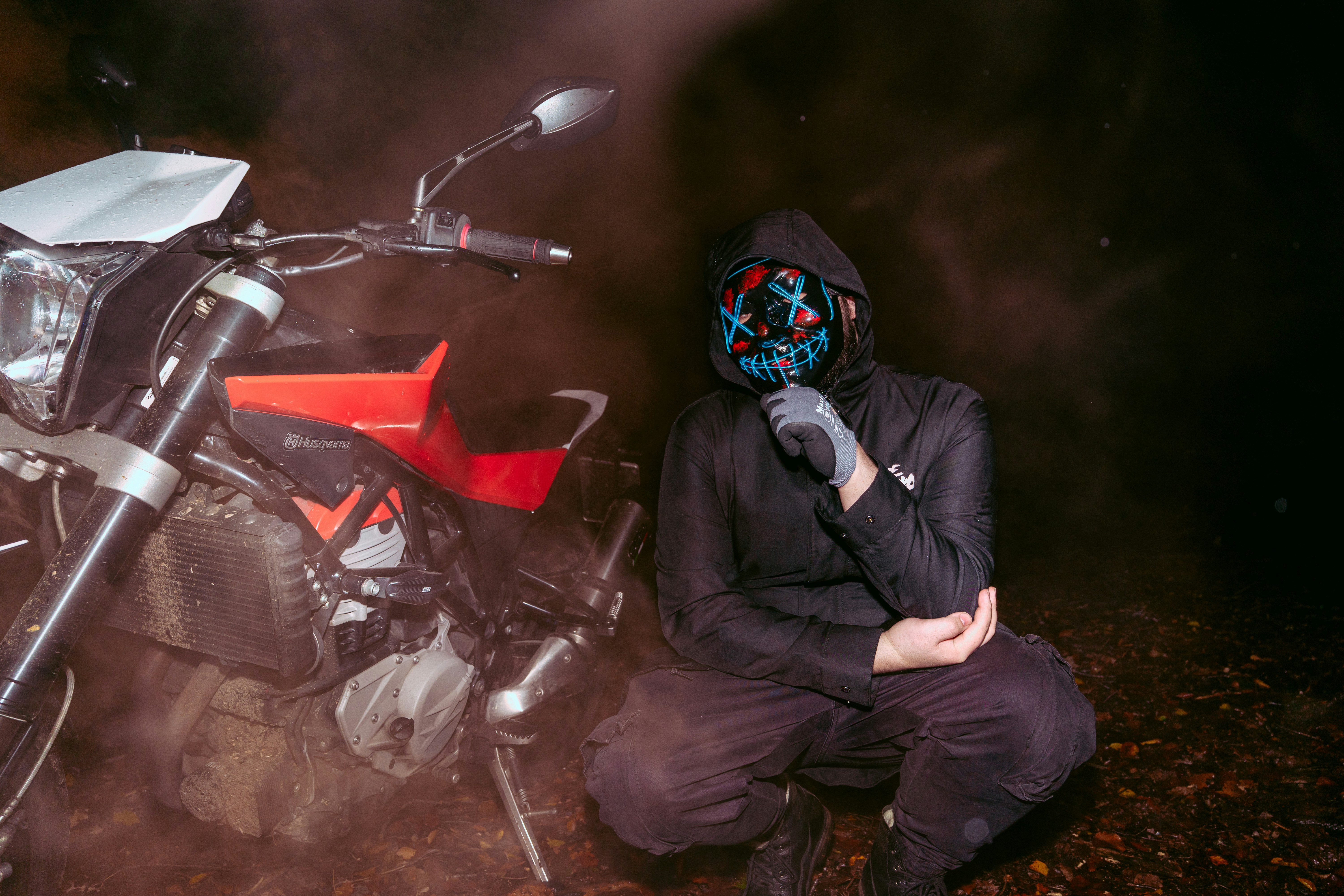 Person in mask and hoodie next to motorcycle