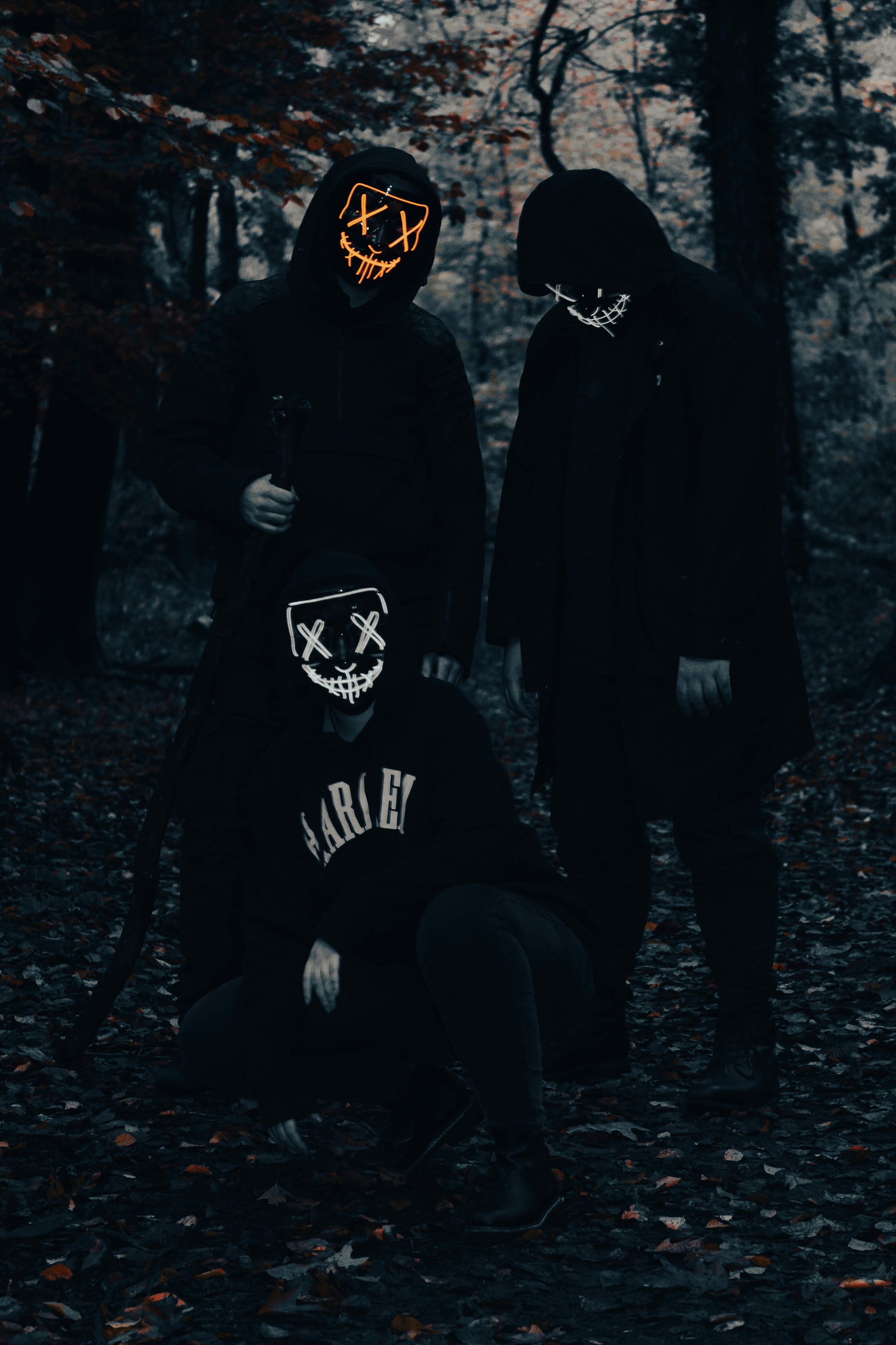 Three people in dark hoodies wearing led masks