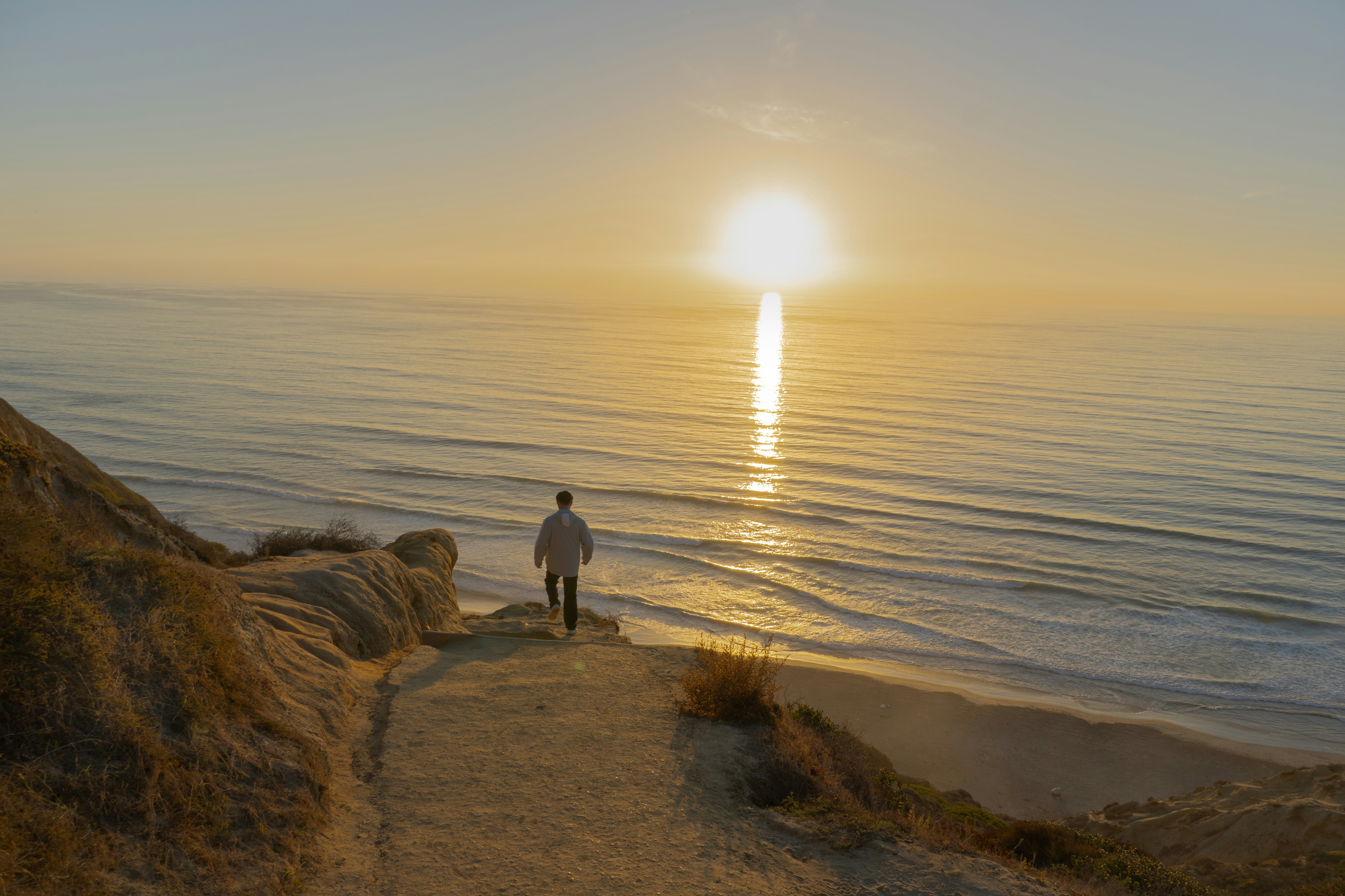 Man walks towards the ocean at sunset
