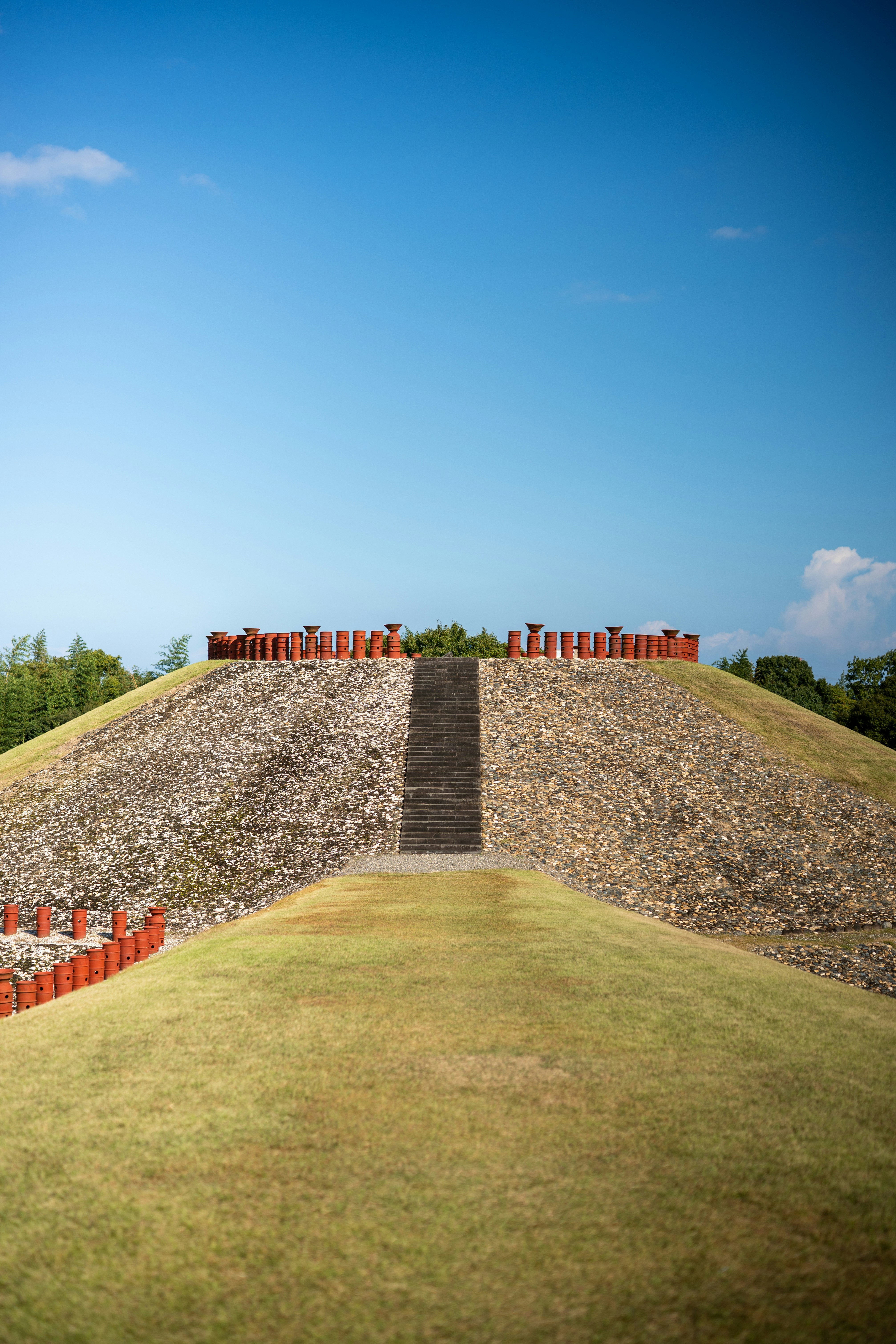 Steinpyramide mit Treppen und roten Säulen unter blauem Himmel