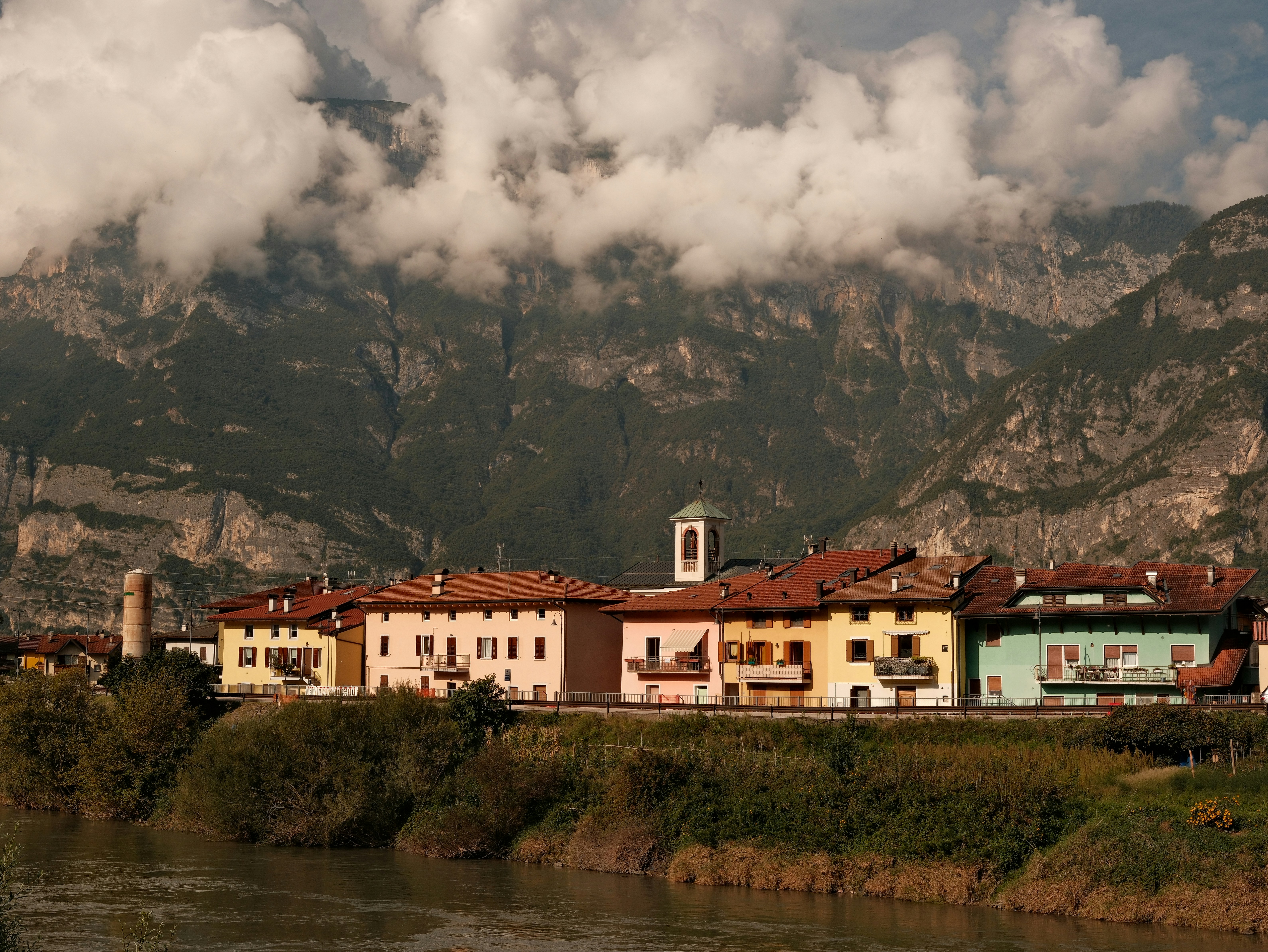 Edifici colorati fiancheggiano un fiume con le montagne alle spalle.