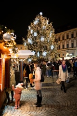 People gather around a large, illuminated christmas tree at night.