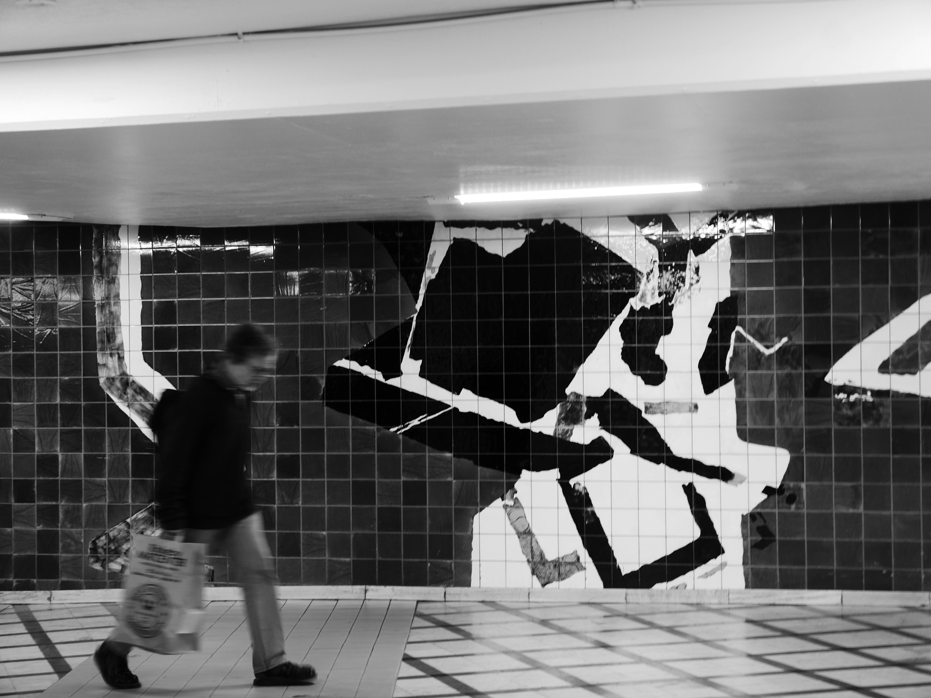 Man walking past abstract mural in subway station.
