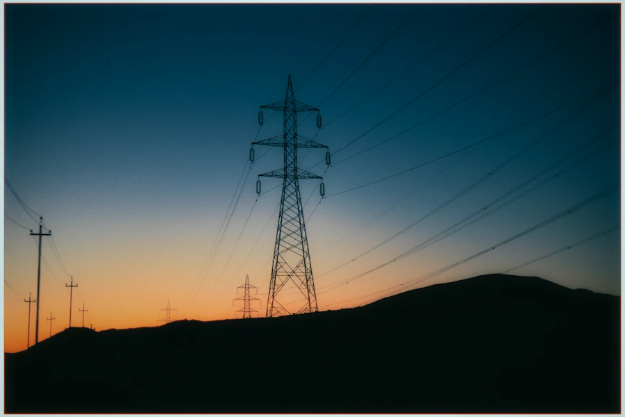 A transmission tower and its lines against a dark blue dusk sky.