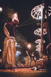Men perform fire ritual at night with decorative lights.