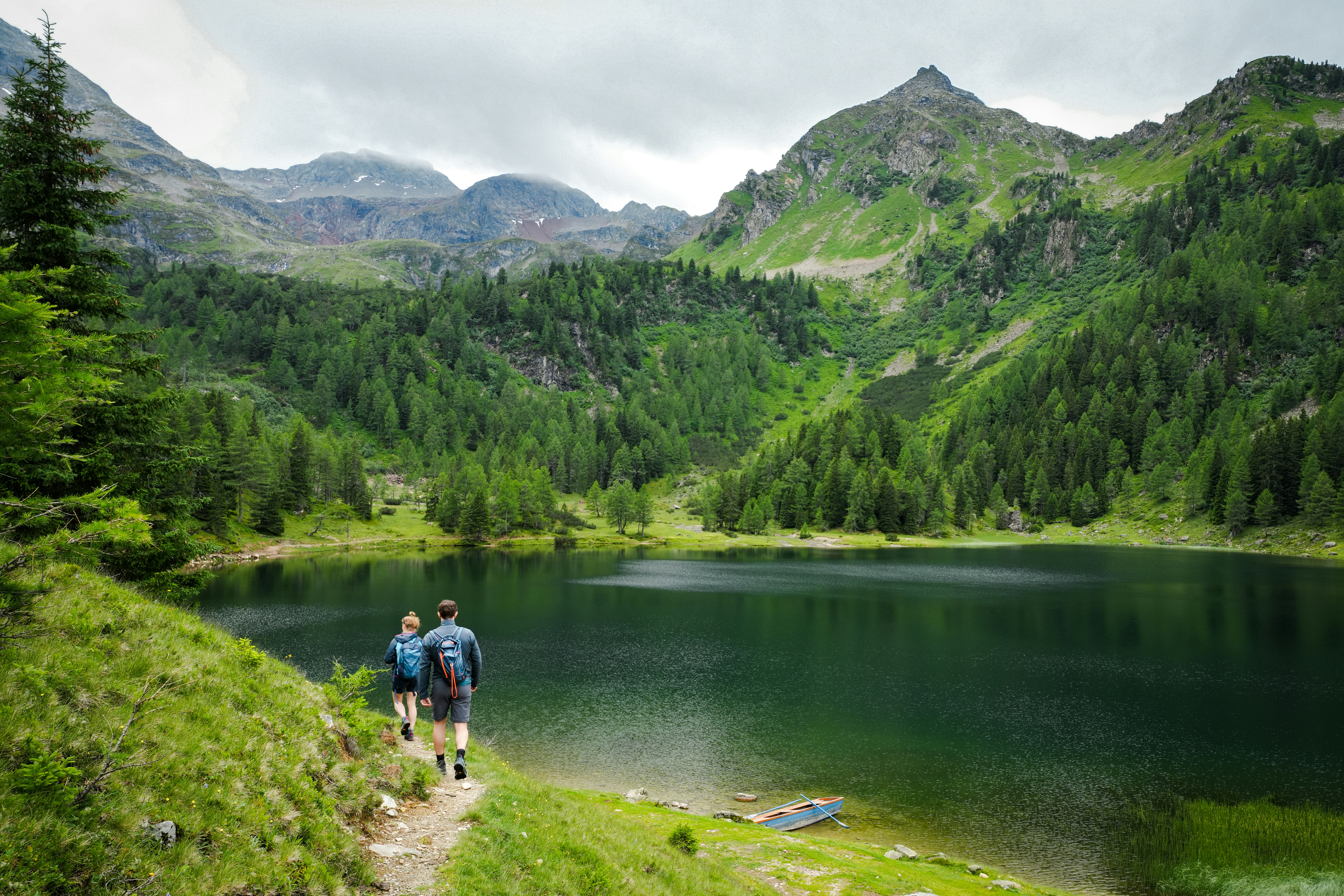 Two hikers walk along a lake in the mountains.