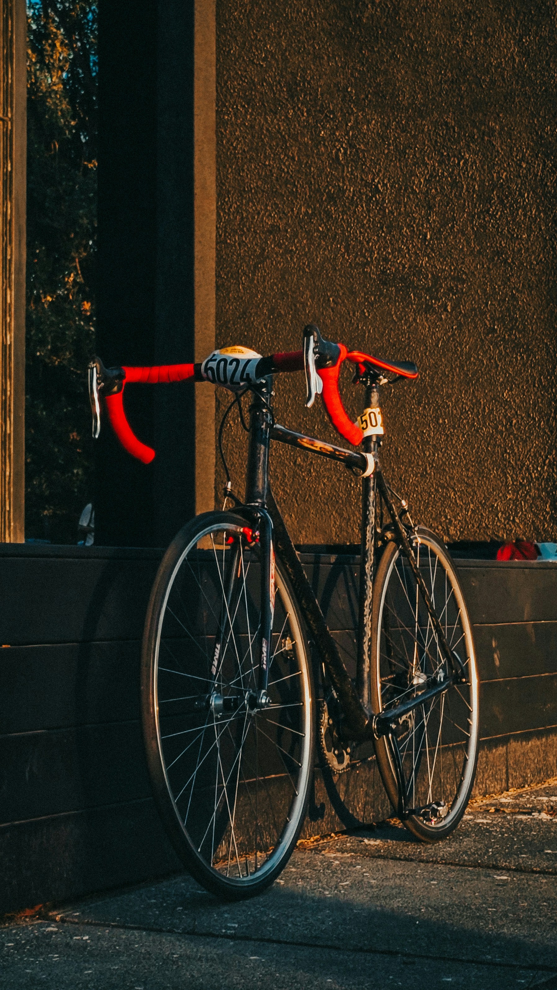 Black racing bicycle with red handlebars parked outdoors.