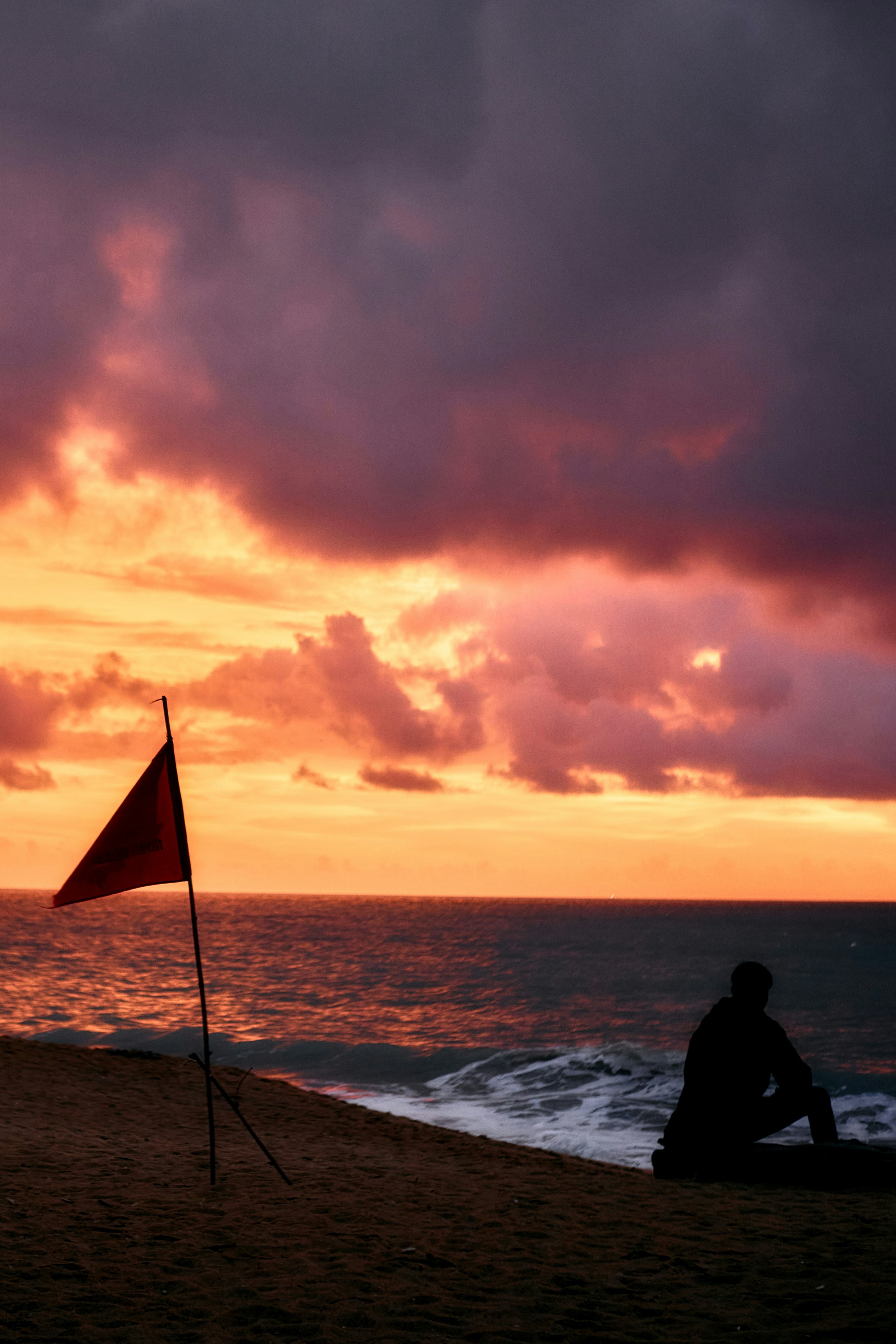 Man watches sunset on beach with red flag.