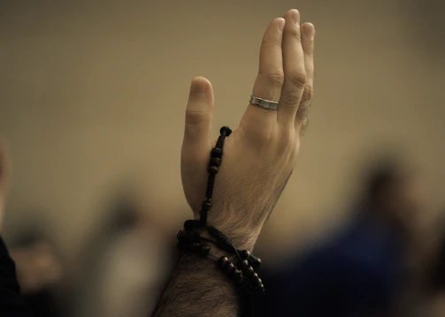 Man's hands holding prayer beads, raised in supplication.