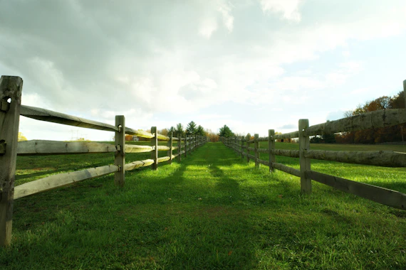 Wooden fence lining a grassy path under cloudy sky.