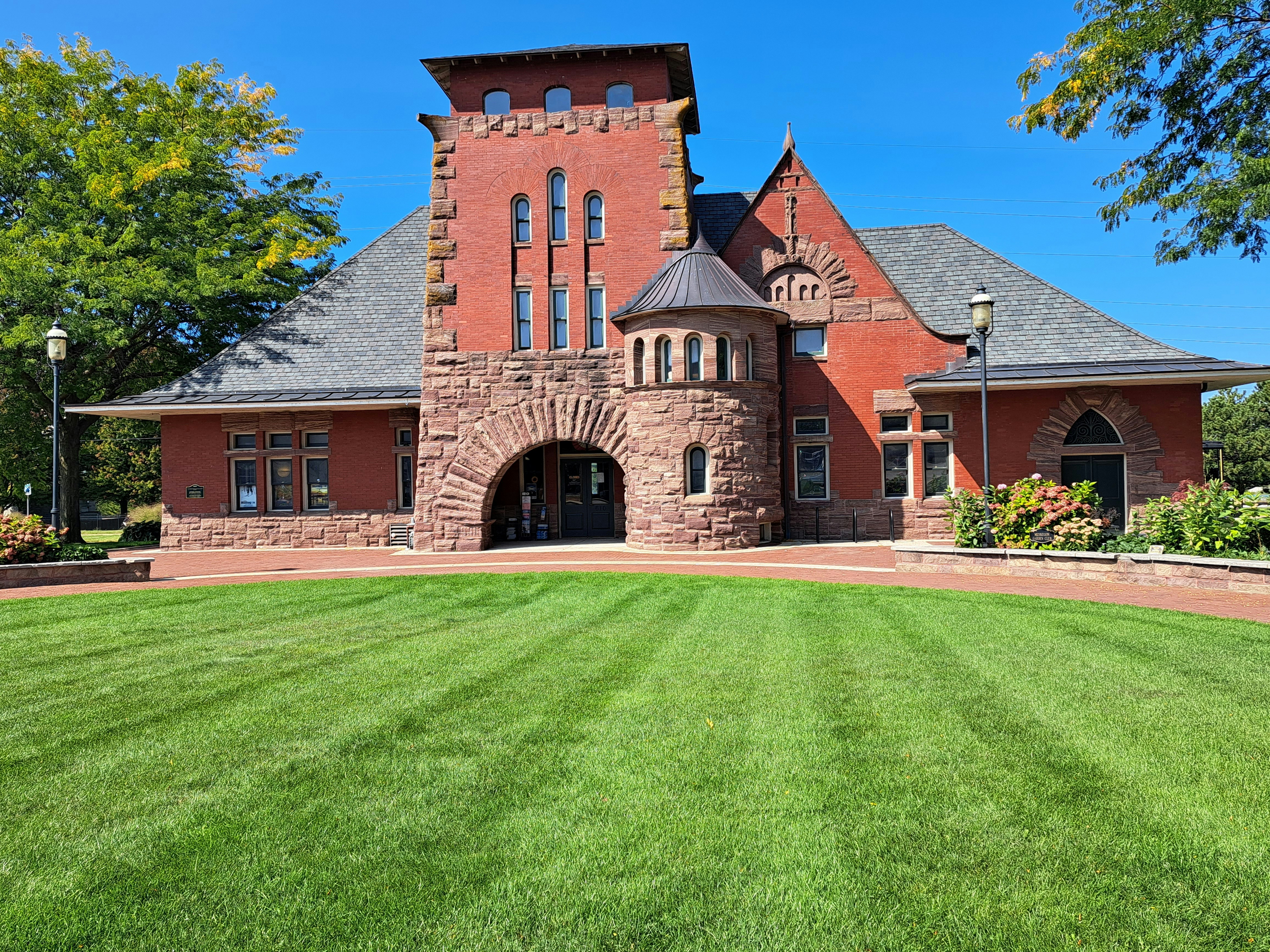 Historischer Bahnhof aus rotem Backstein mit rundem Türmchen.