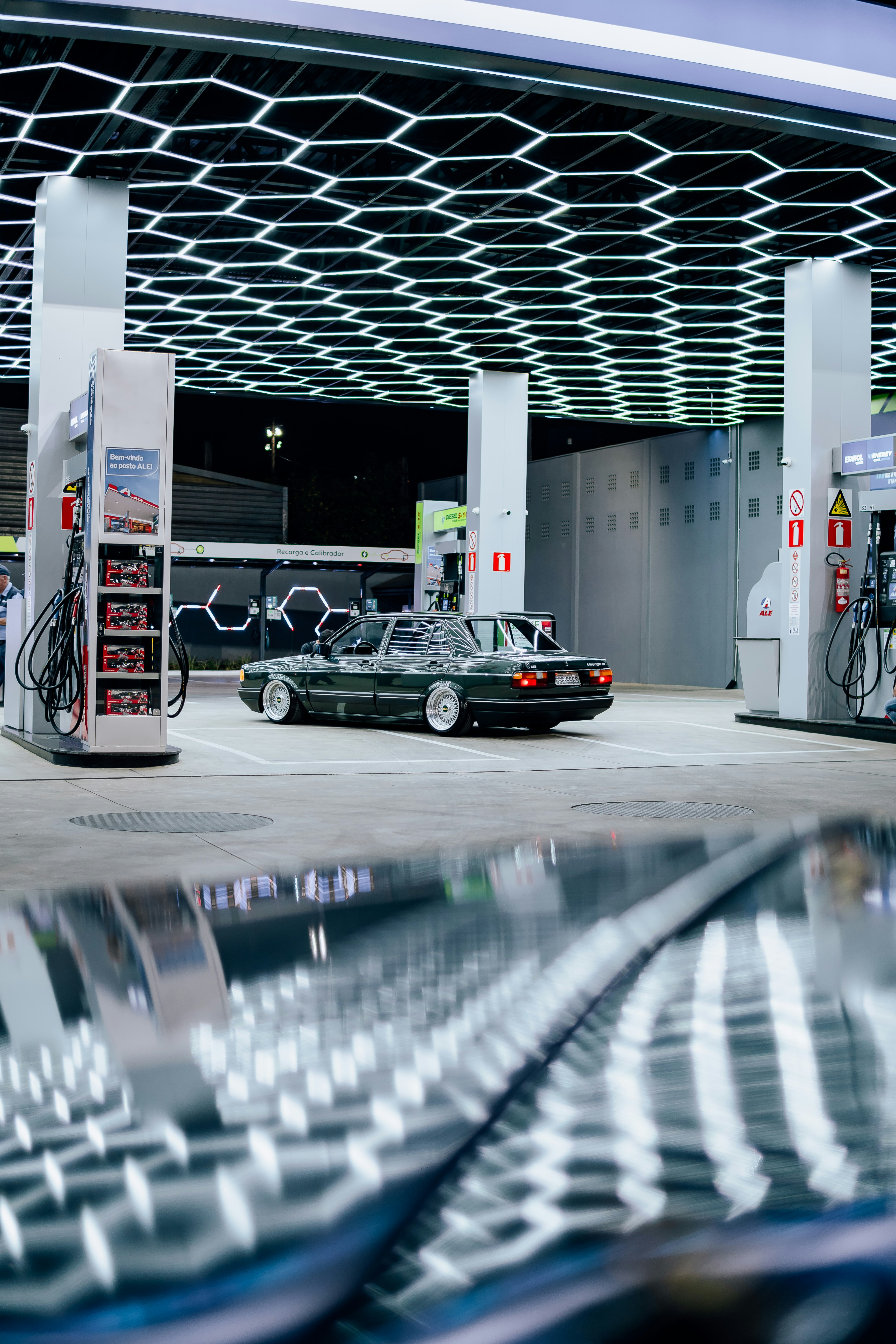 A vintage car at a modern gas station at night.