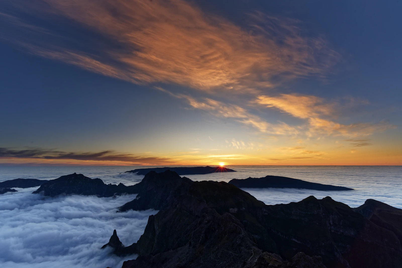 Sunrise over a sea of clouds above mountain peaks