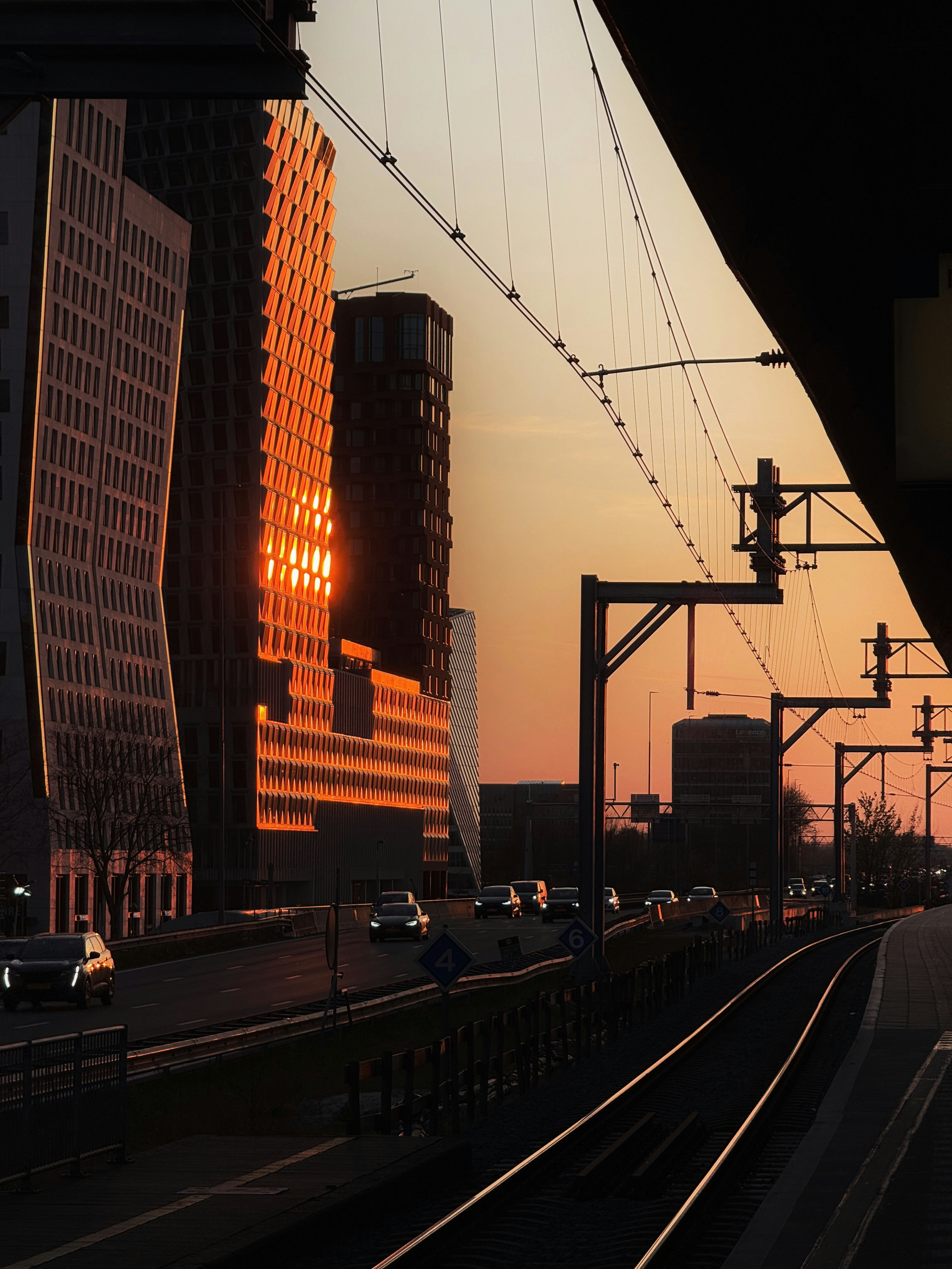 Modern buildings reflecting sunset light over busy road.