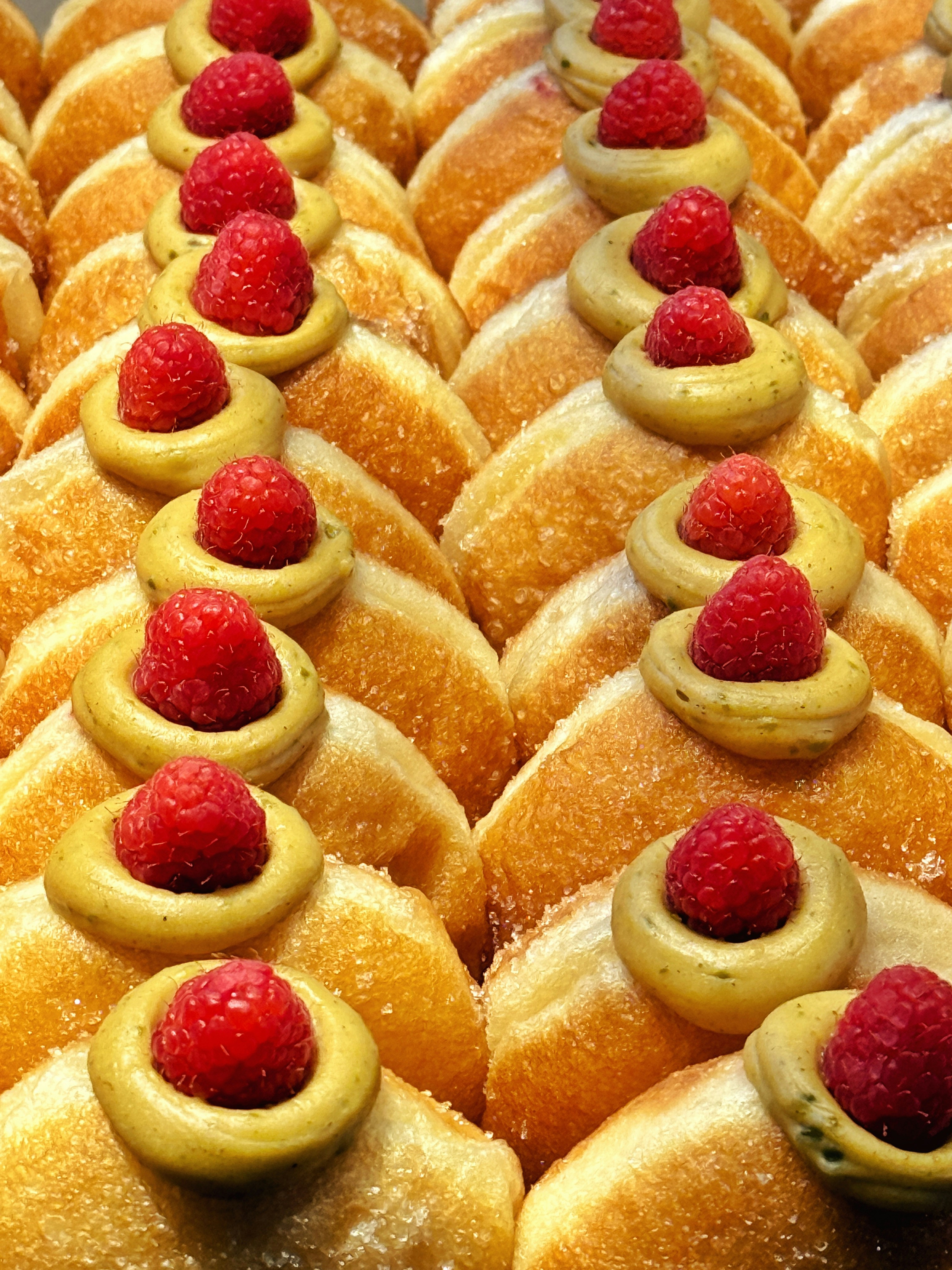 Rows of donuts topped with raspberries and frosting
