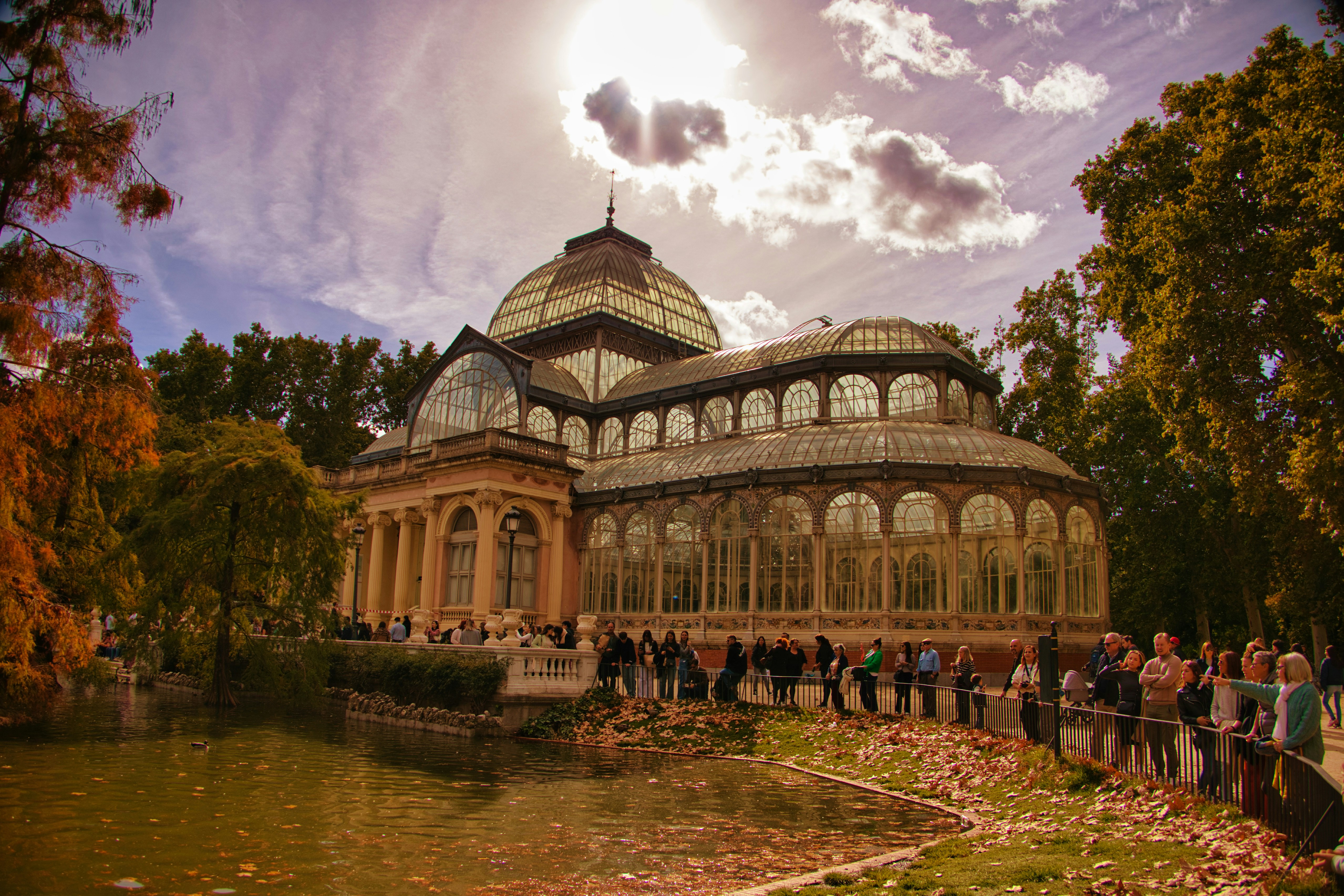 Glass palace surrounded by trees and a pond.