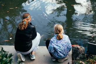 Two girls squatting by a calm pond