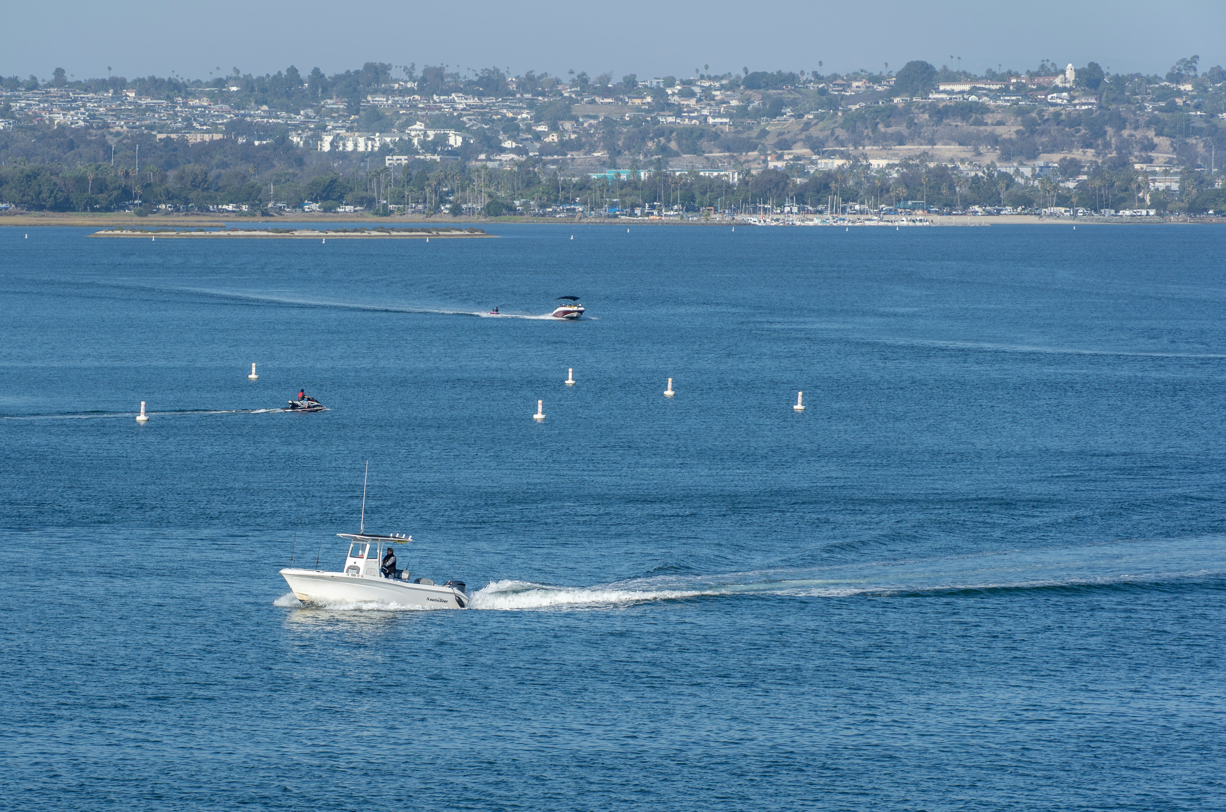 Boats sailing on a wide blue bay with distant city.