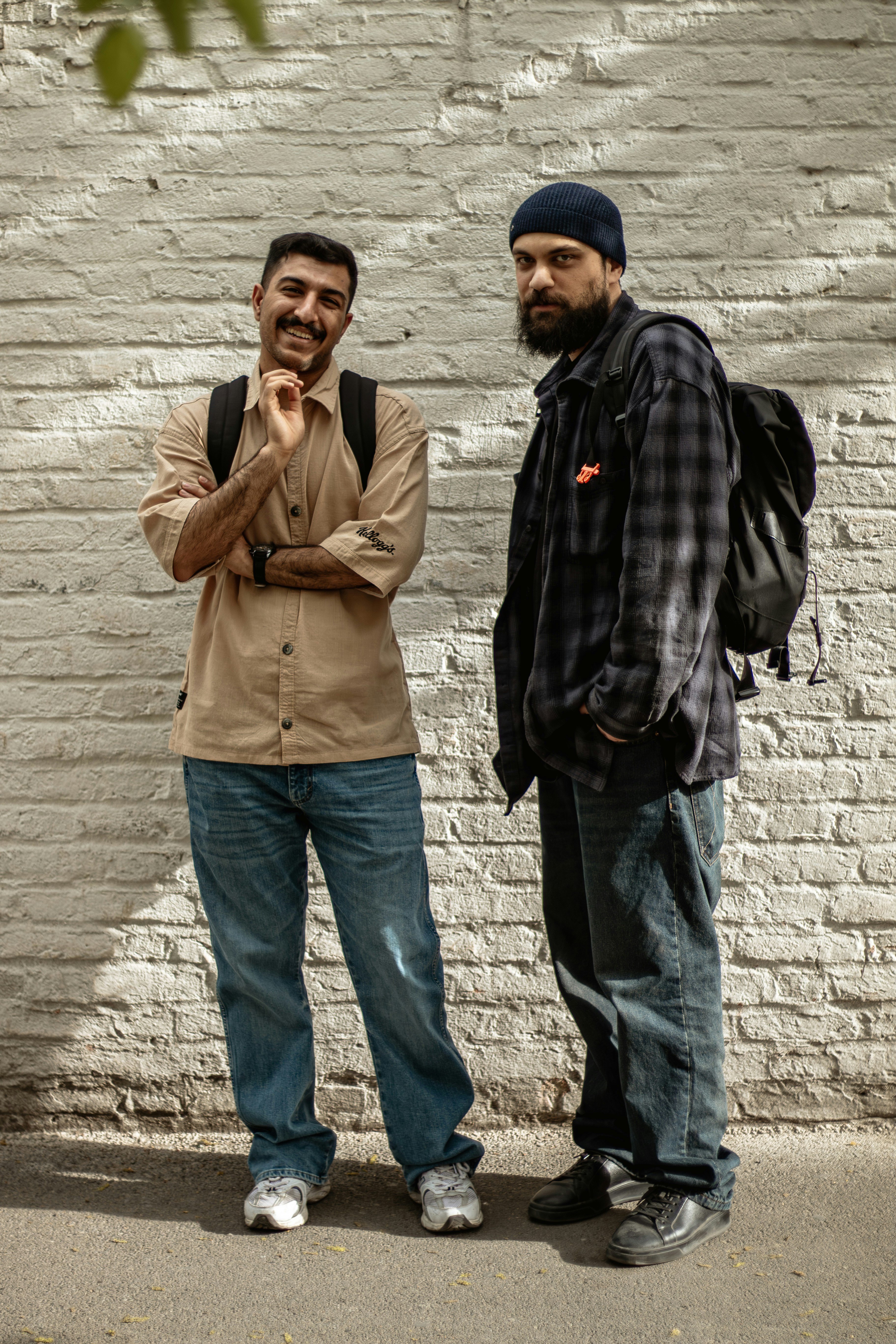 Two men standing against a white brick wall