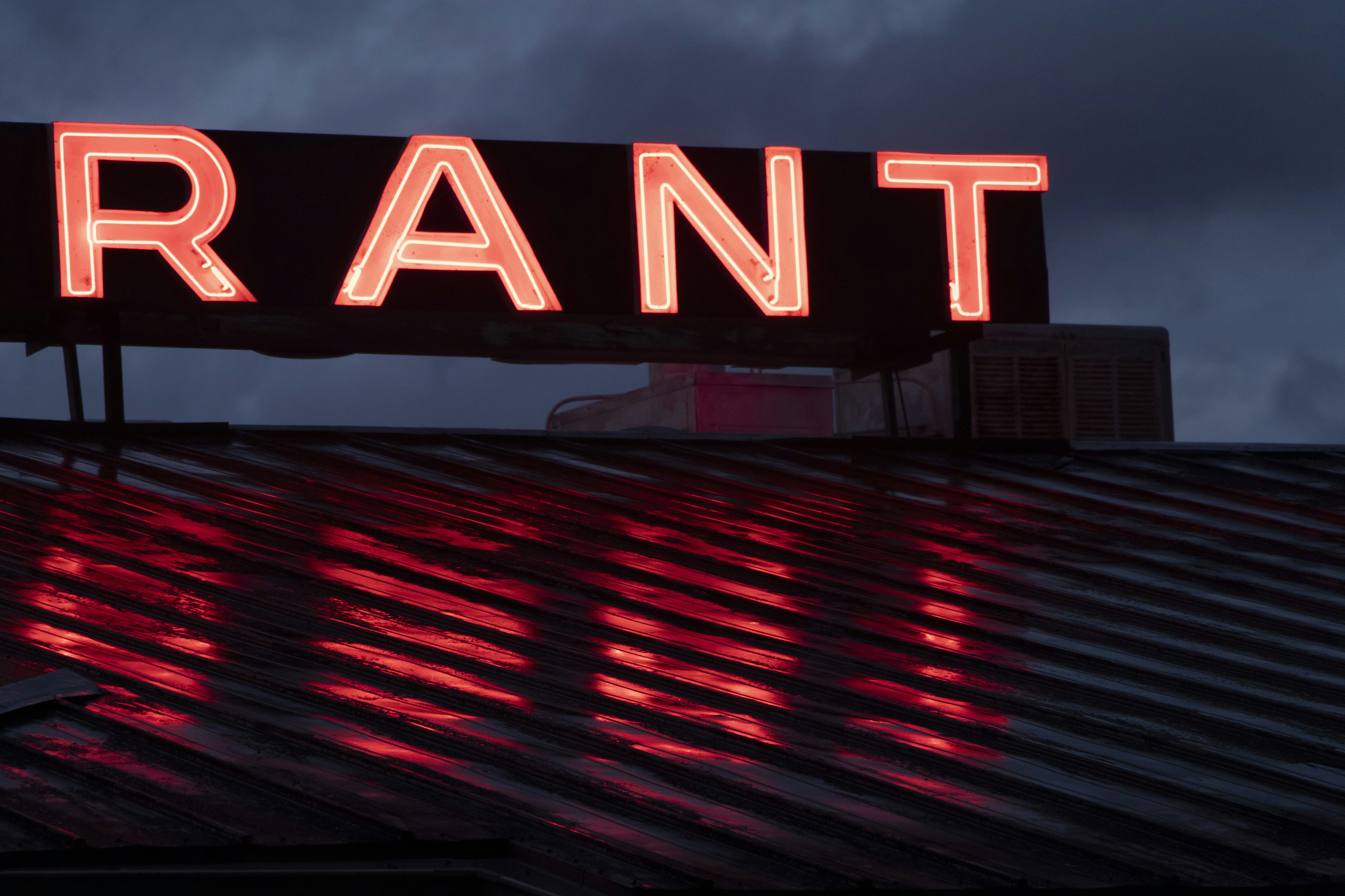 Neon 'rant' sign reflects on wet roof at night