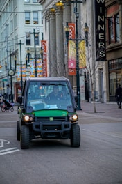 Green utility vehicle driving on a city street.