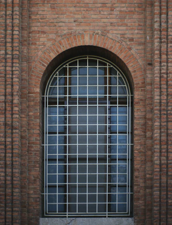 Arched window with white bars on brick wall