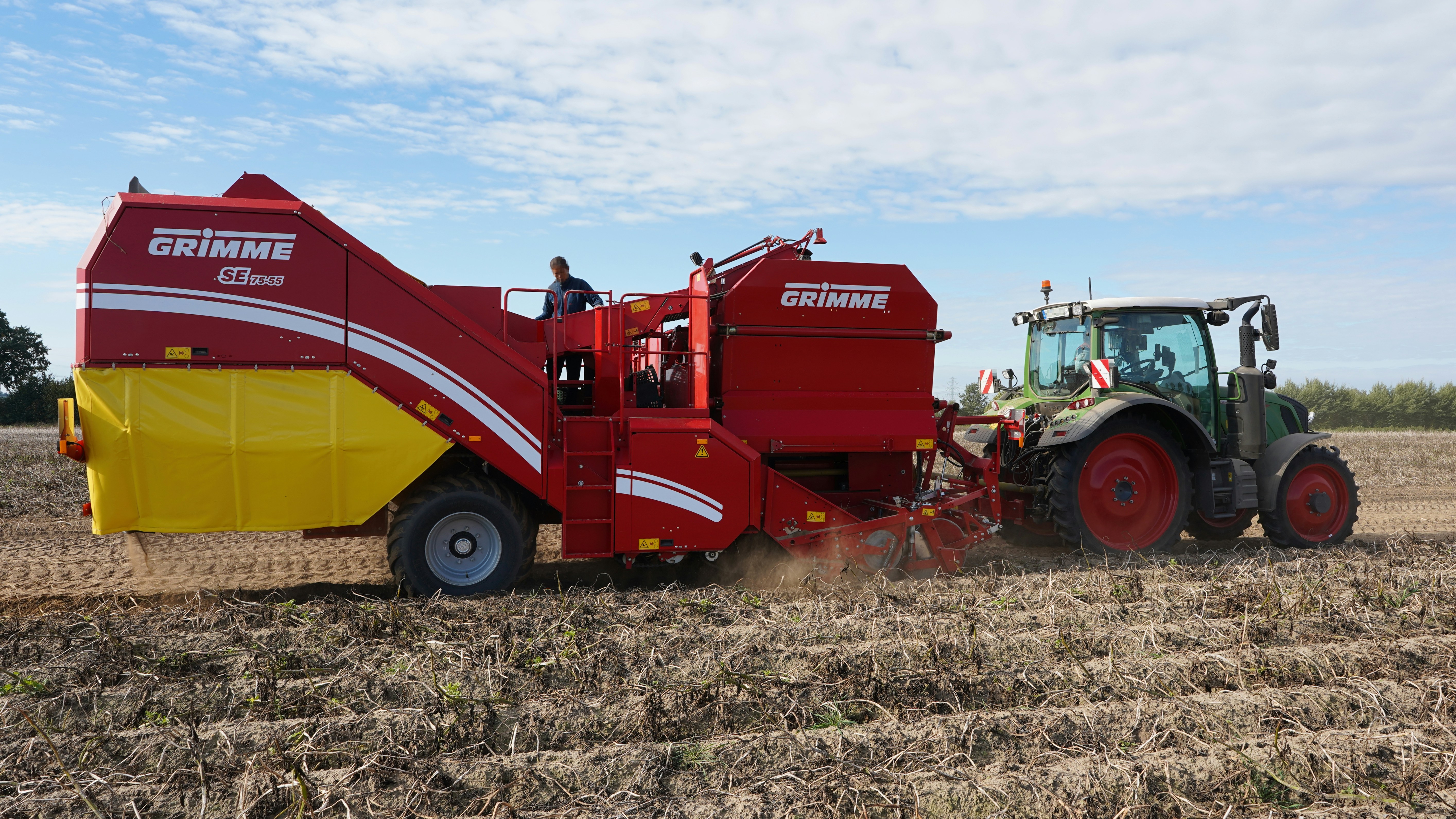 Tractor pulling a potato harvester in a field.