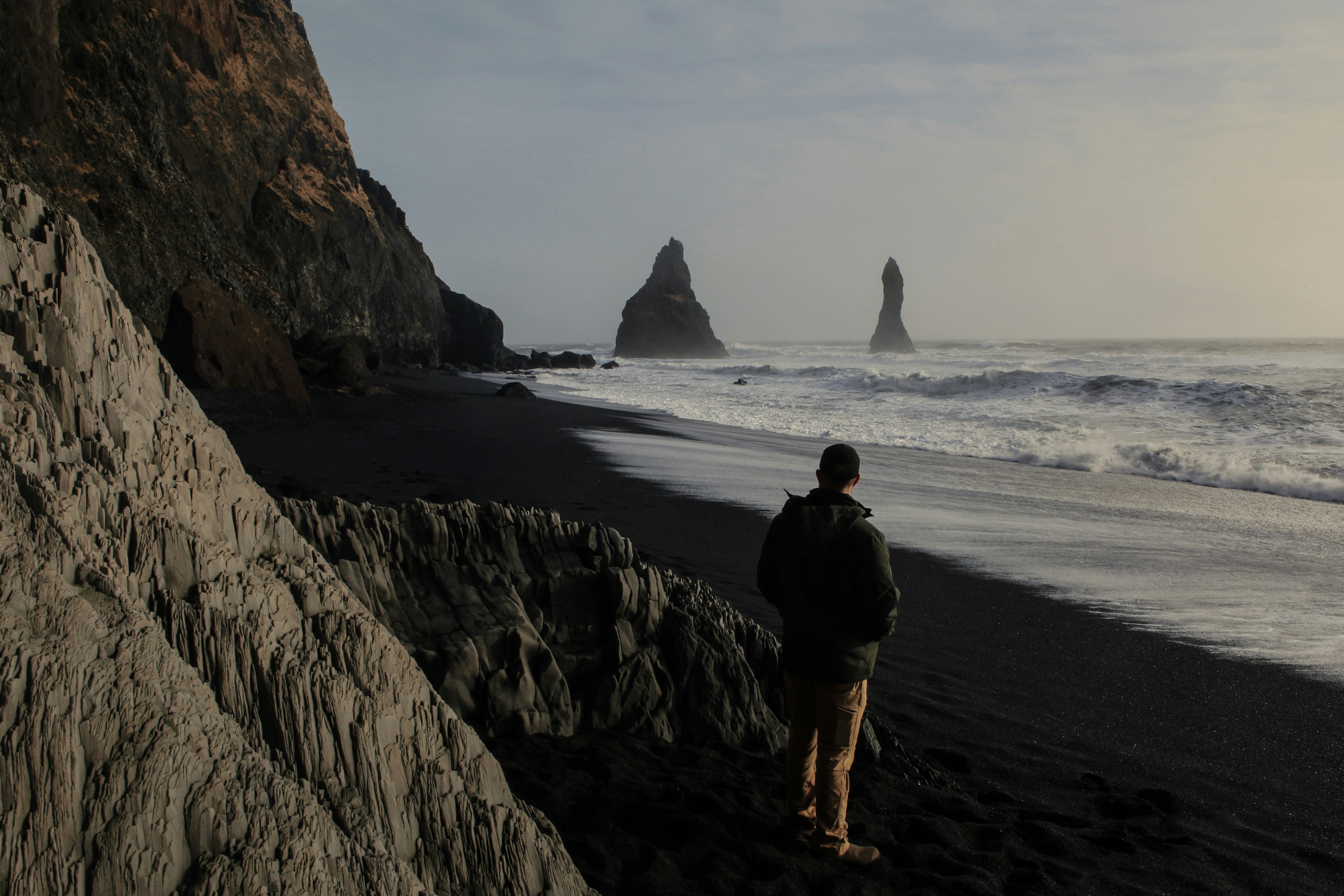 Uomo in piedi sulla spiaggia di sabbia nera con faraglioni.