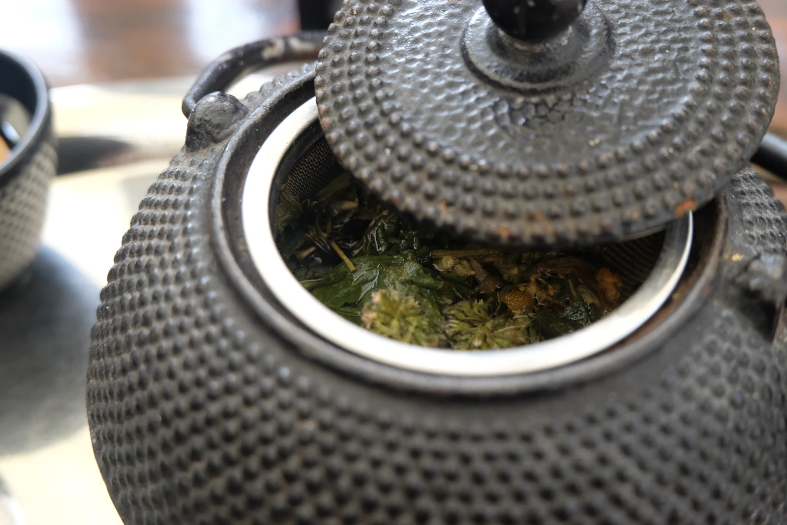 Hobnail cast-iron teapot with its lid lifted over loose-leaf tea