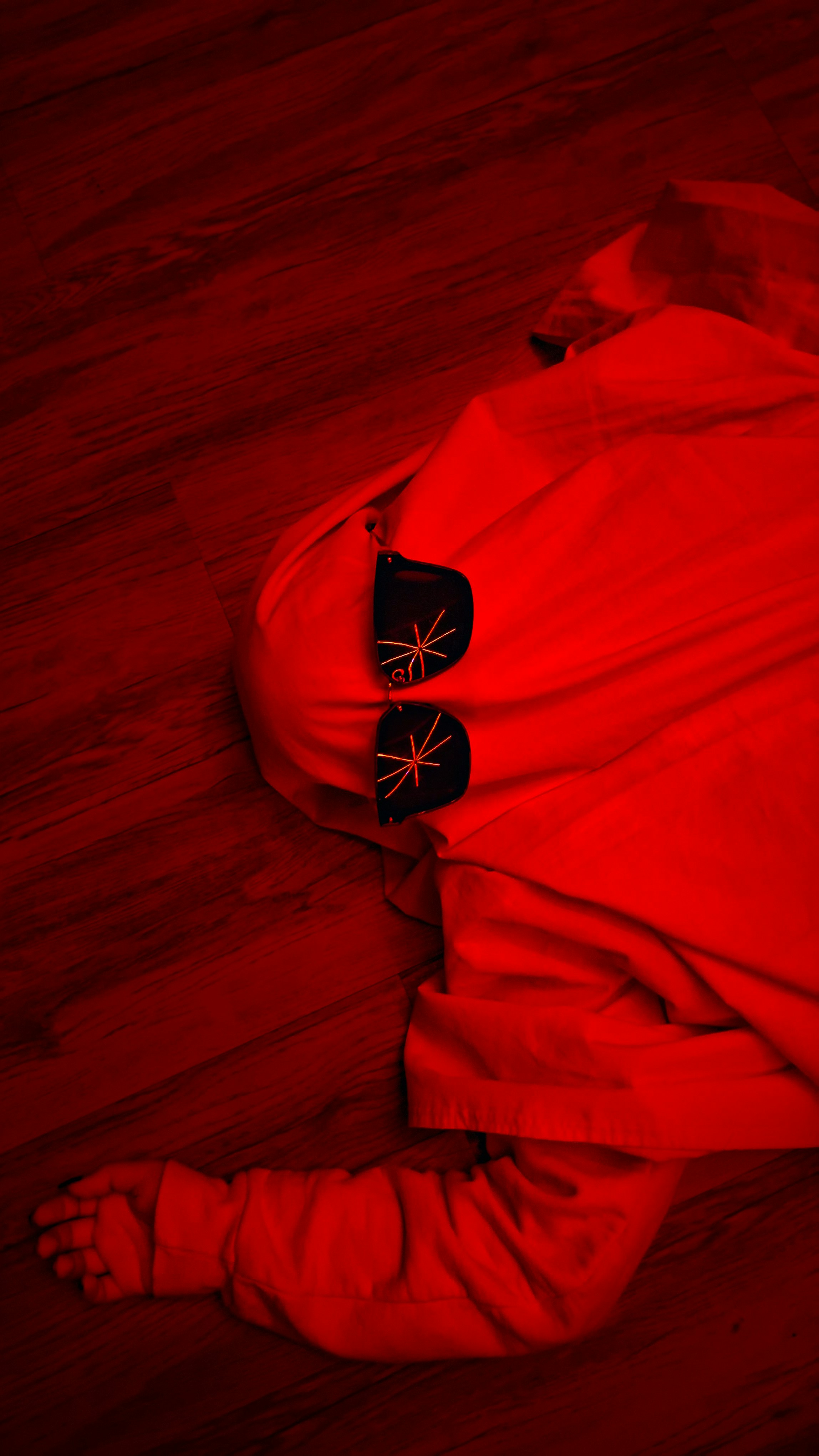 Part of a photo series — see more on my profile! A surreal red-lit scene depicting a human figure draped in fabric, lying motionless on a wooden floor. The glowing red tones evoke themes of exhaustion, identity, and emotional detachment — blurring the line between performance and reality, horror and reflection. Perfect for concepts like surrealism, identity loss, or the human condition in modern art photography. Model featured gave full consent for photography and Unsplash publication. Model’s face is intentionally covered for privacy.