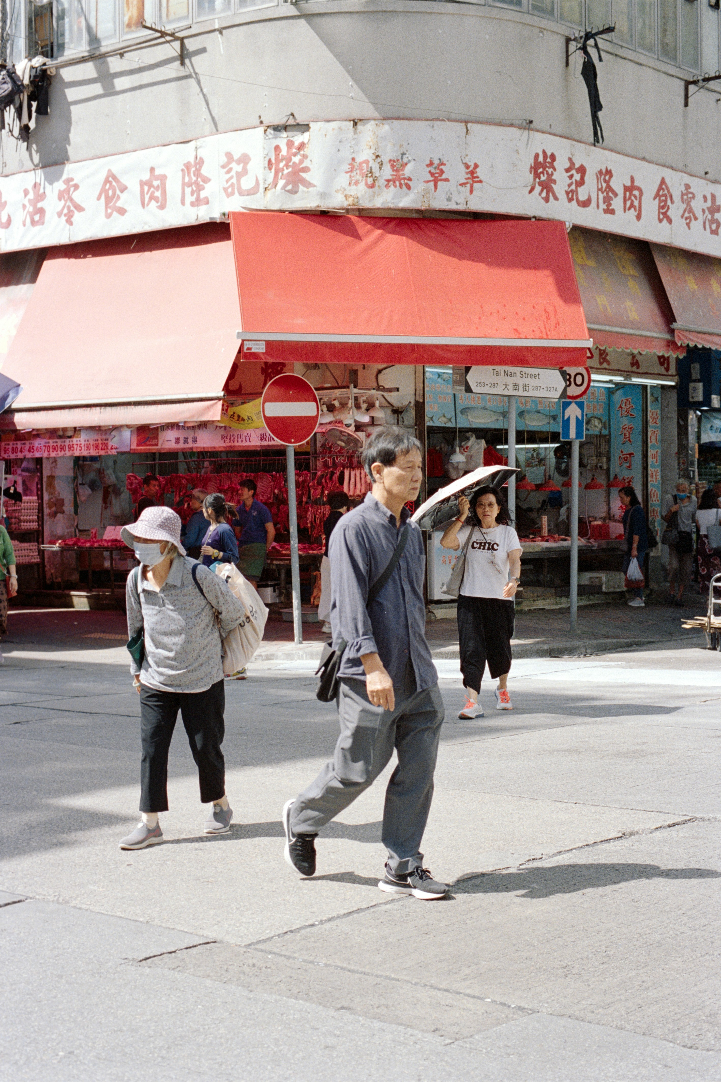 People walk on a sunny street in front of shops.