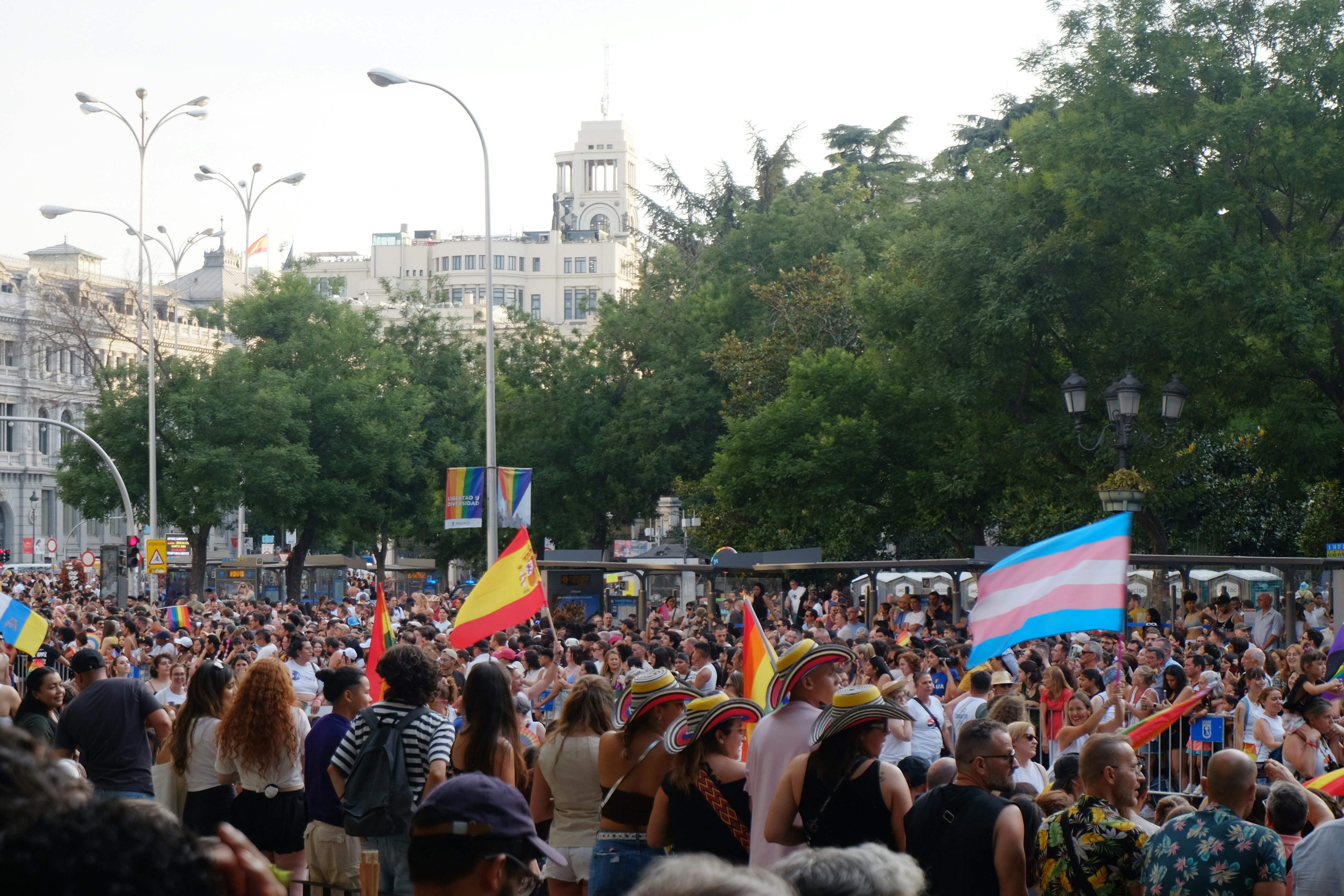 Menschenmenge bei einer Parade mit spanischen und Transgender-Flaggen.