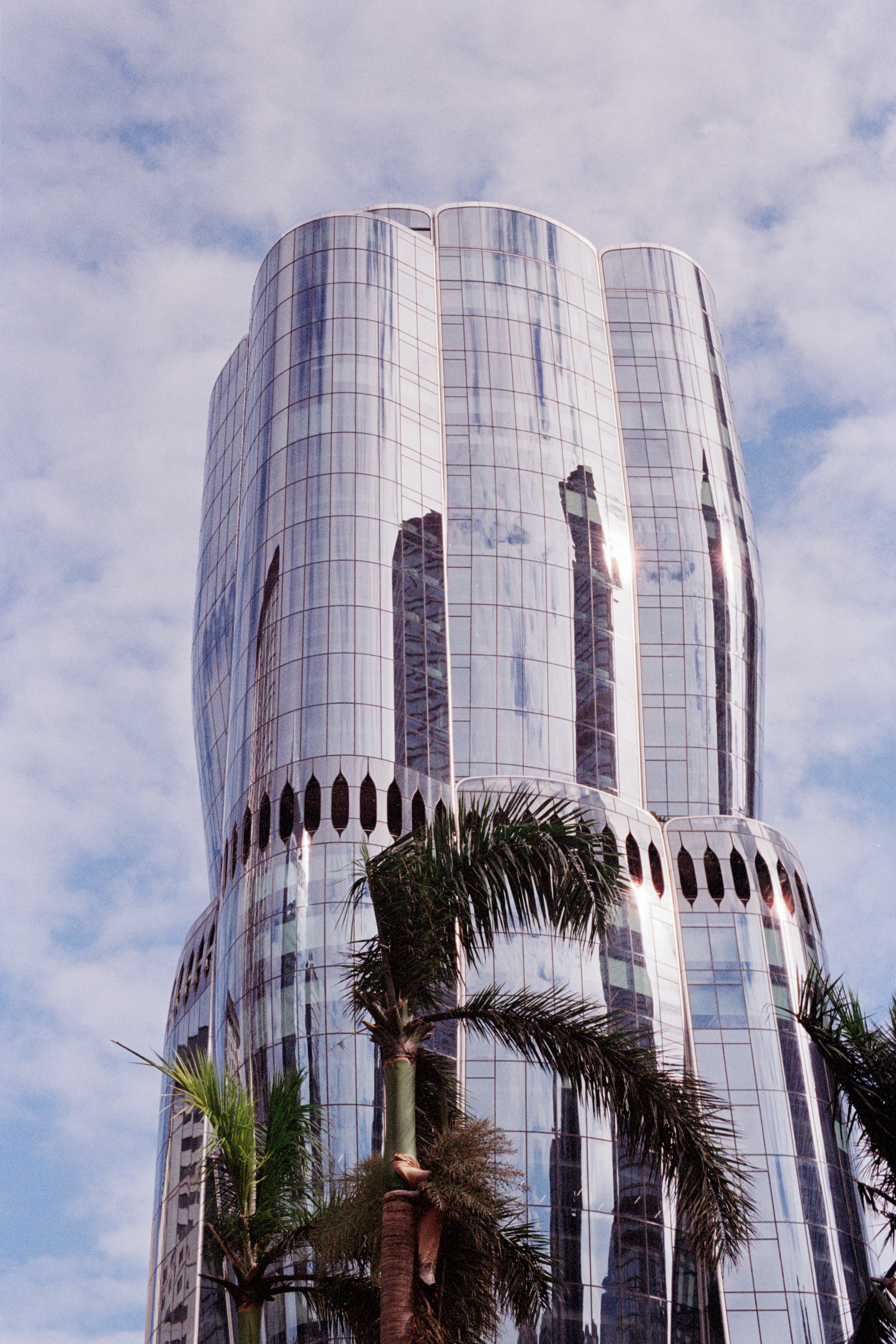 Moderno rascacielos de cristal con palmeras y cielo.