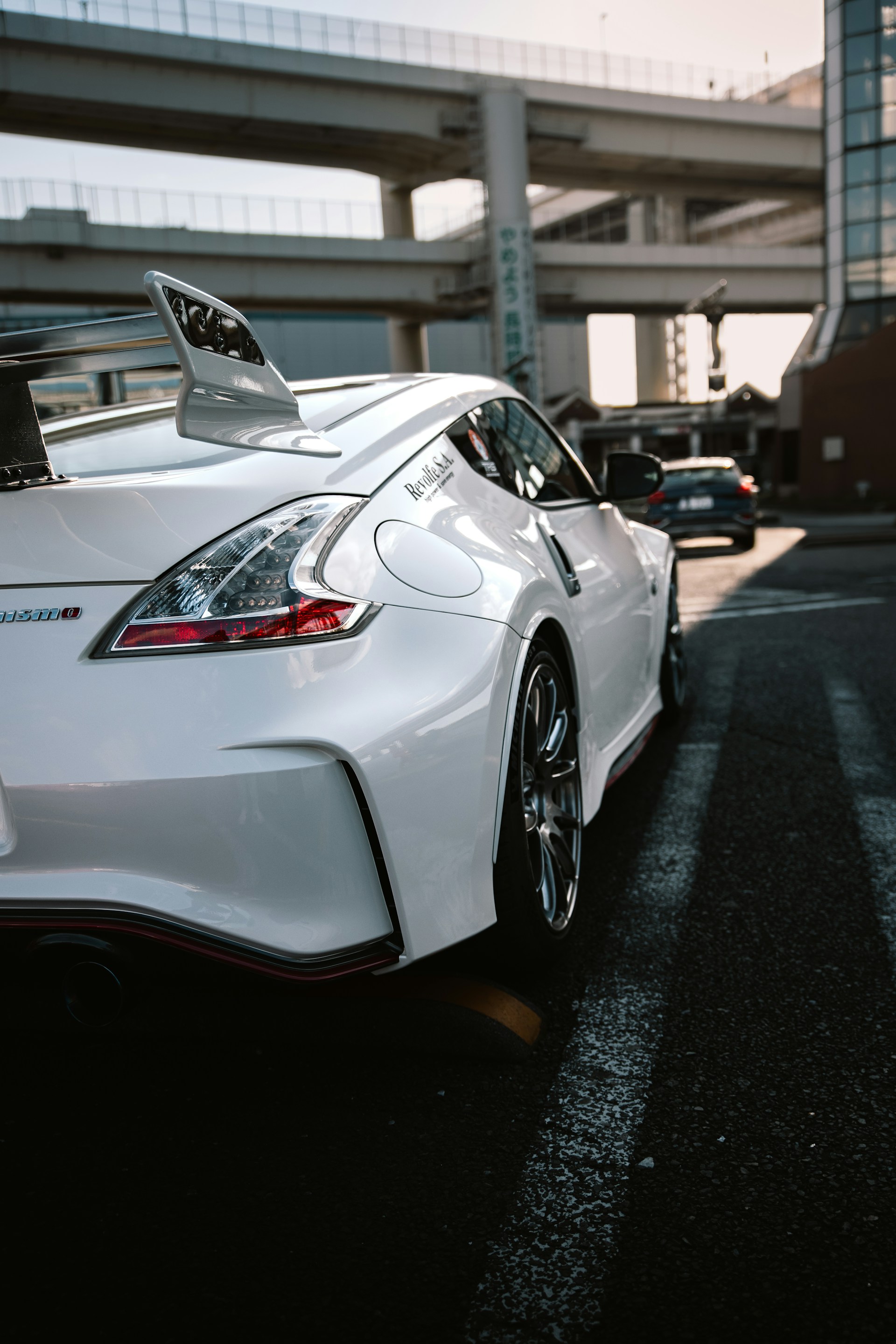 White sports car parked on street with highway overpass.